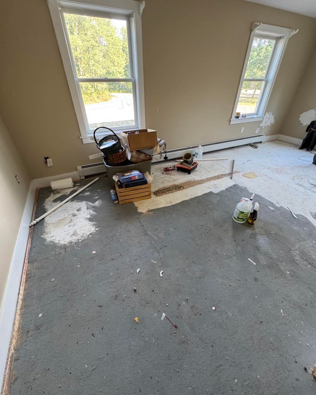 Renovated room with gray carpet, white plastic sheeting, tools, and supplies by two windows