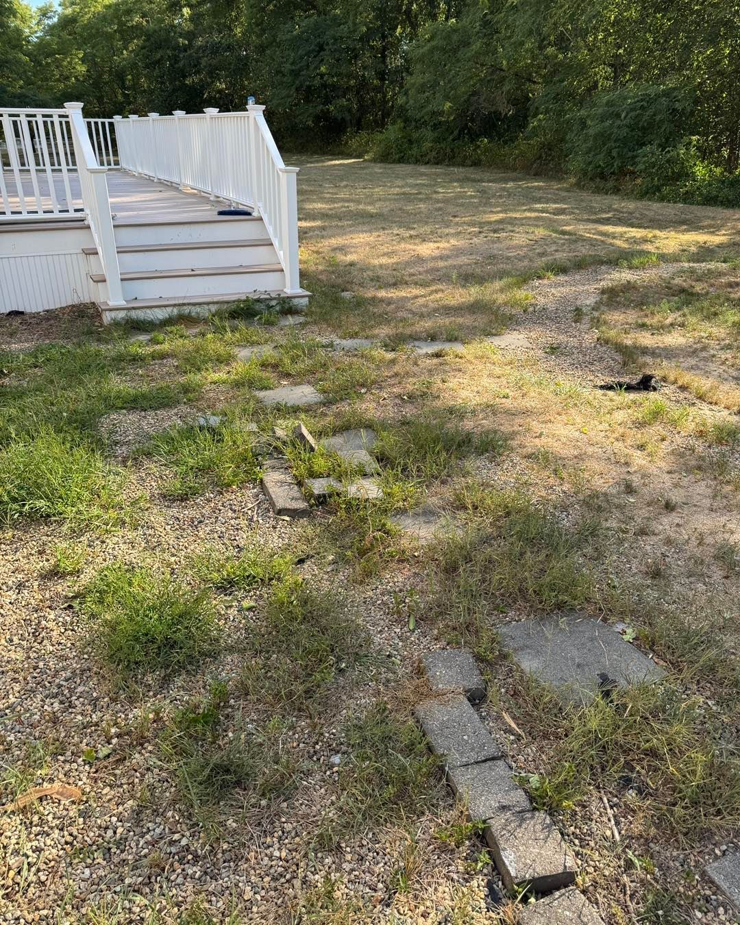 White porch steps beside a patchy grassy yard with scattered pavers and trees in the background