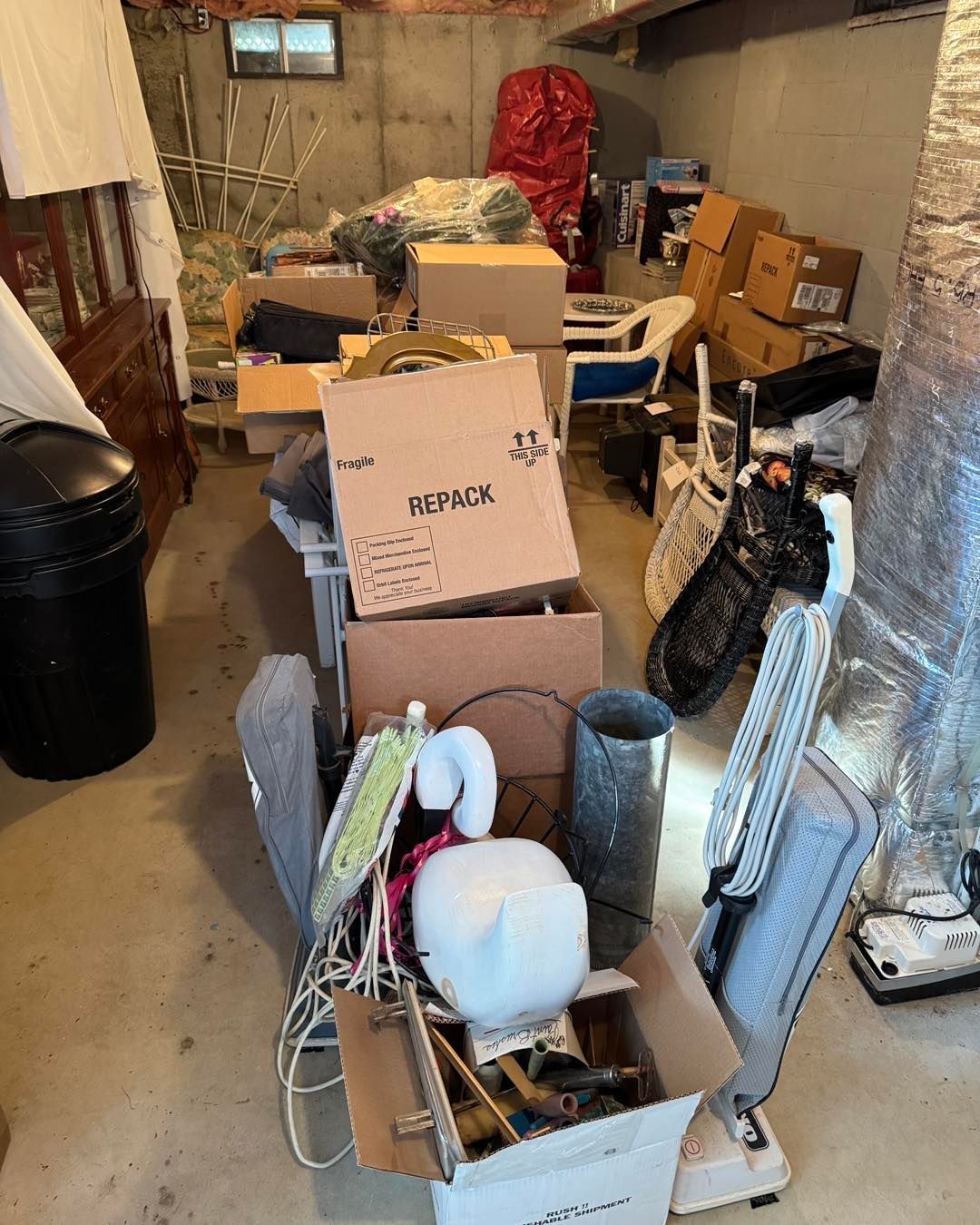 Cluttered basement storage area with open boxes, tools, and household items stacked along a narrow walkway