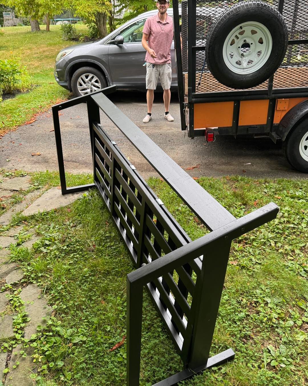 Black metal railing ramp beside a trailer, with a man and parked car in a grassy driveway.
