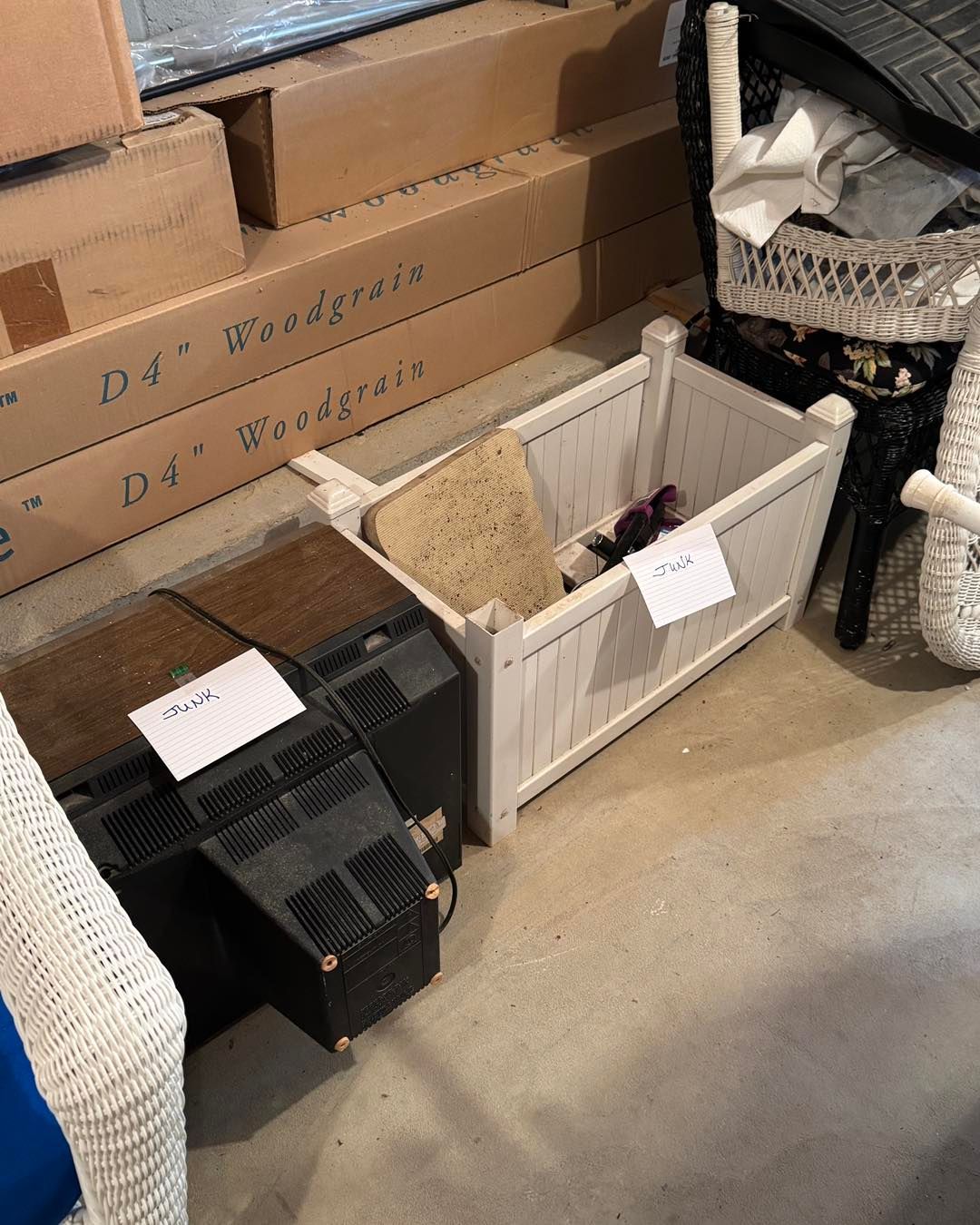 Storage area with boxes, black crate, and white bin holding assorted items on a concrete floor.