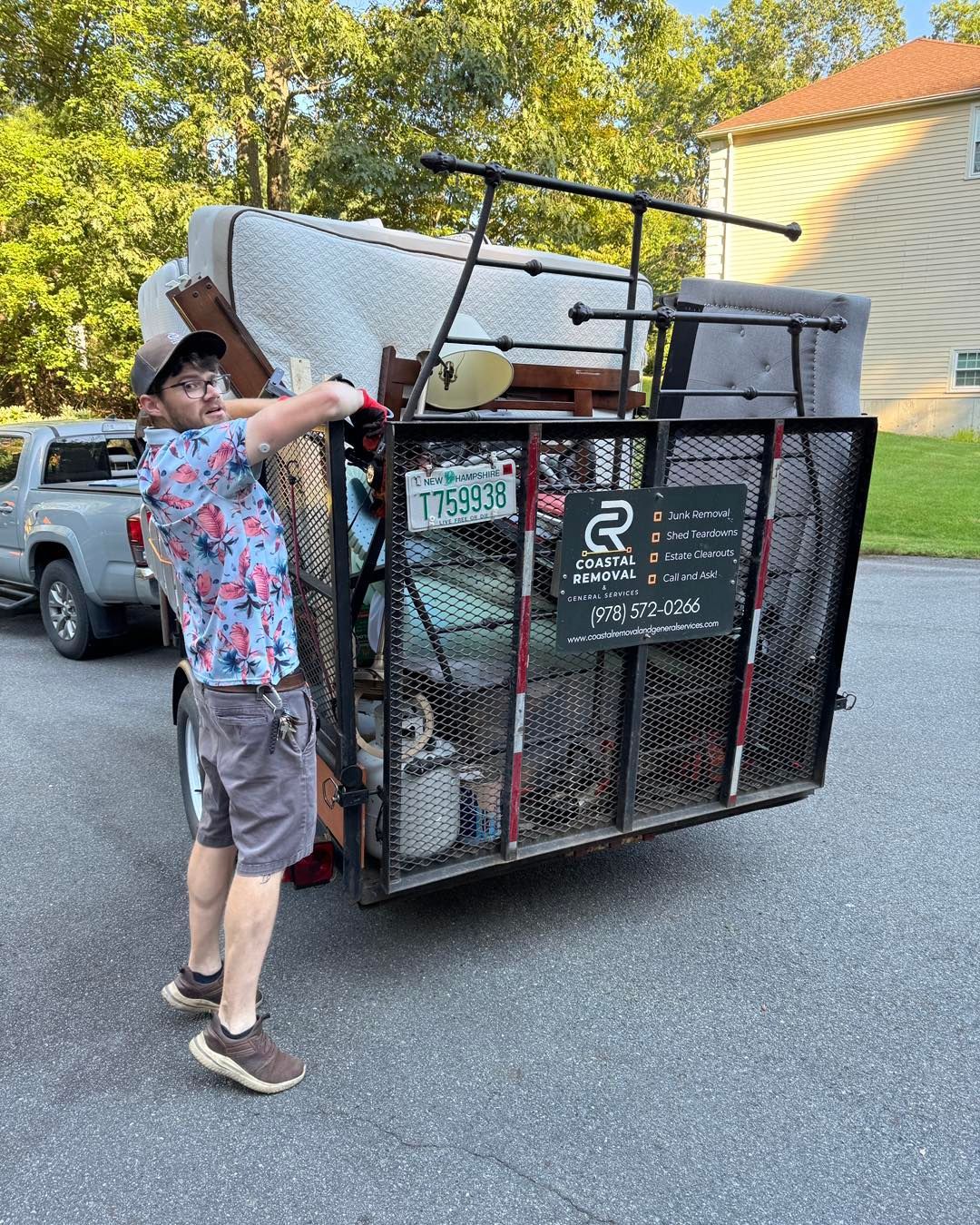 Person pulling a loaded metal cart with furniture and bags beside a parked truck outdoors