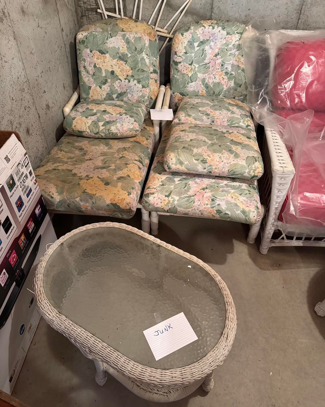 Small floral chair set in a storage room, with an empty wicker basket in front and a pink chair to the side.
