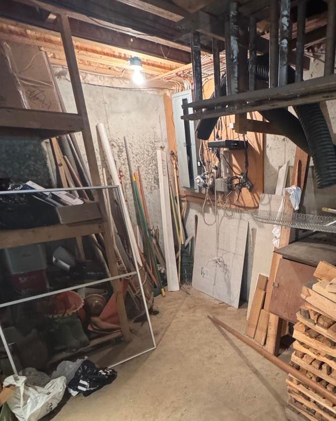 Cluttered basement workshop with lumber, shelves, tools, and stacked wooden pallets