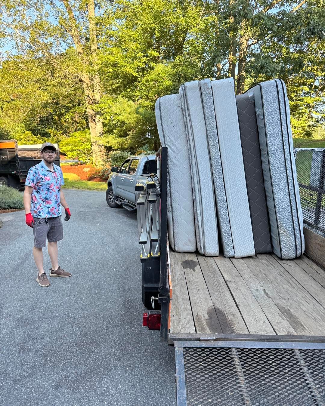 Person beside a truck carrying stacked mattresses on a gravel road near trees