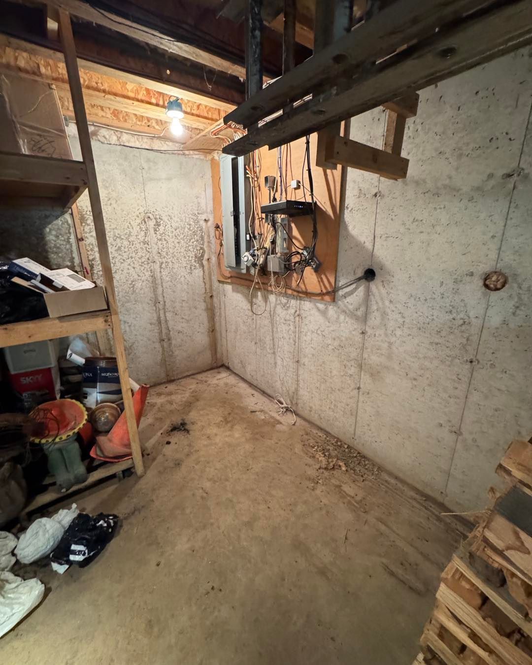 Empty unfinished basement room with concrete walls, exposed beams, shelves, and a small window opening.
