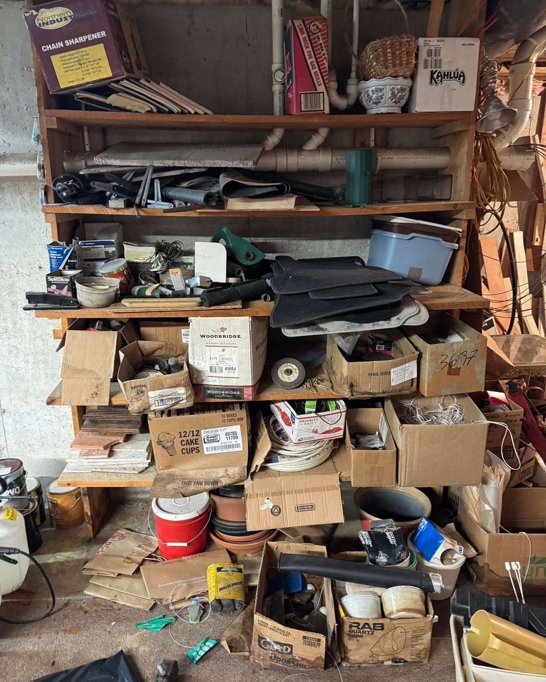 Cluttered storage shelf filled with boxes, tools, jars, and miscellaneous household items