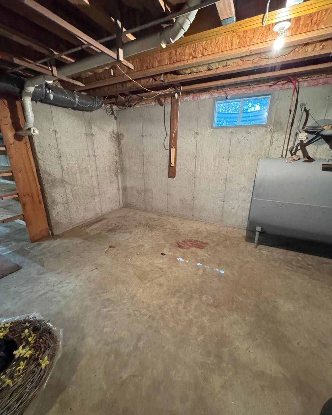 Empty unfinished basement with concrete walls, exposed beams, and a small window.