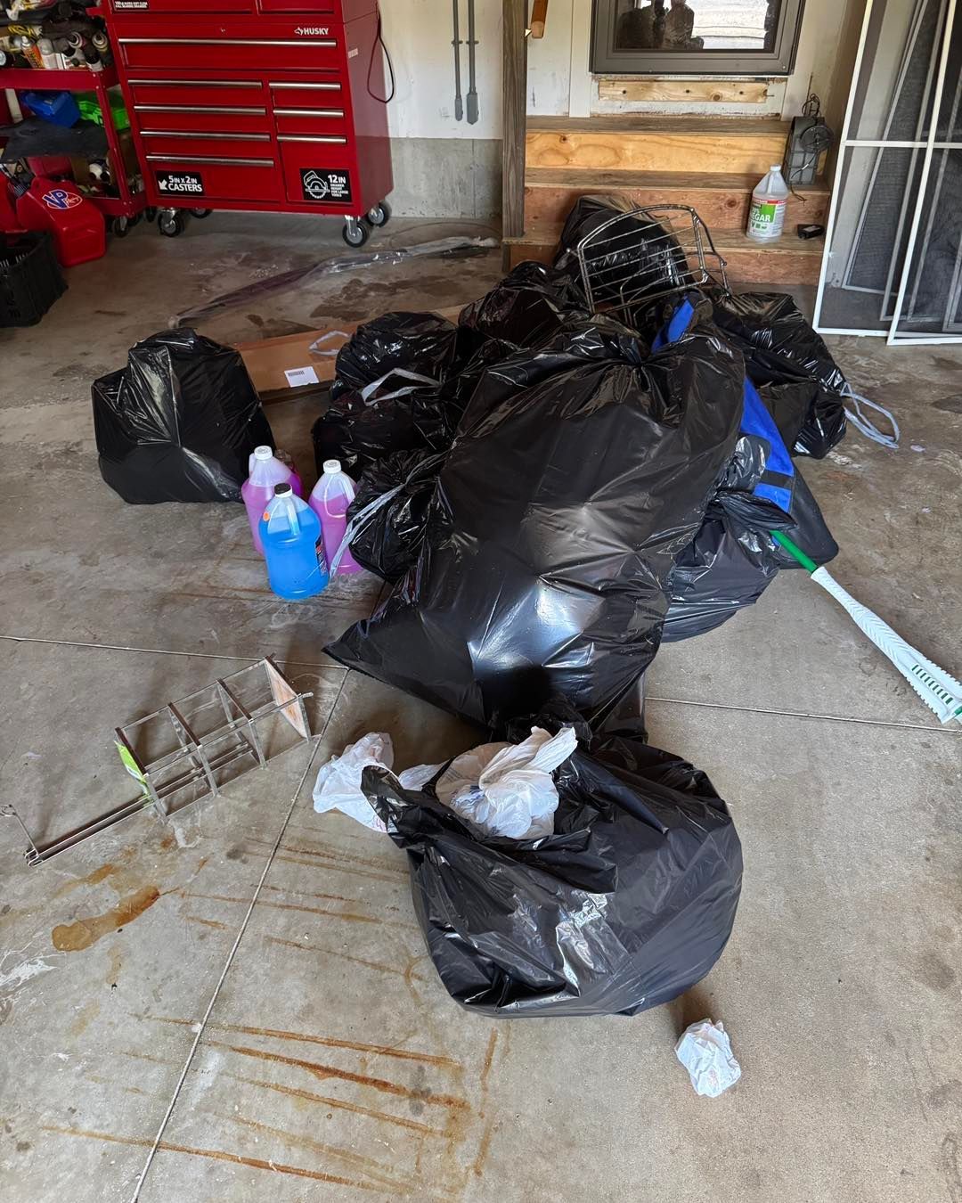 Pile of black trash bags and scattered items on a garage floor beside a red tool chest.