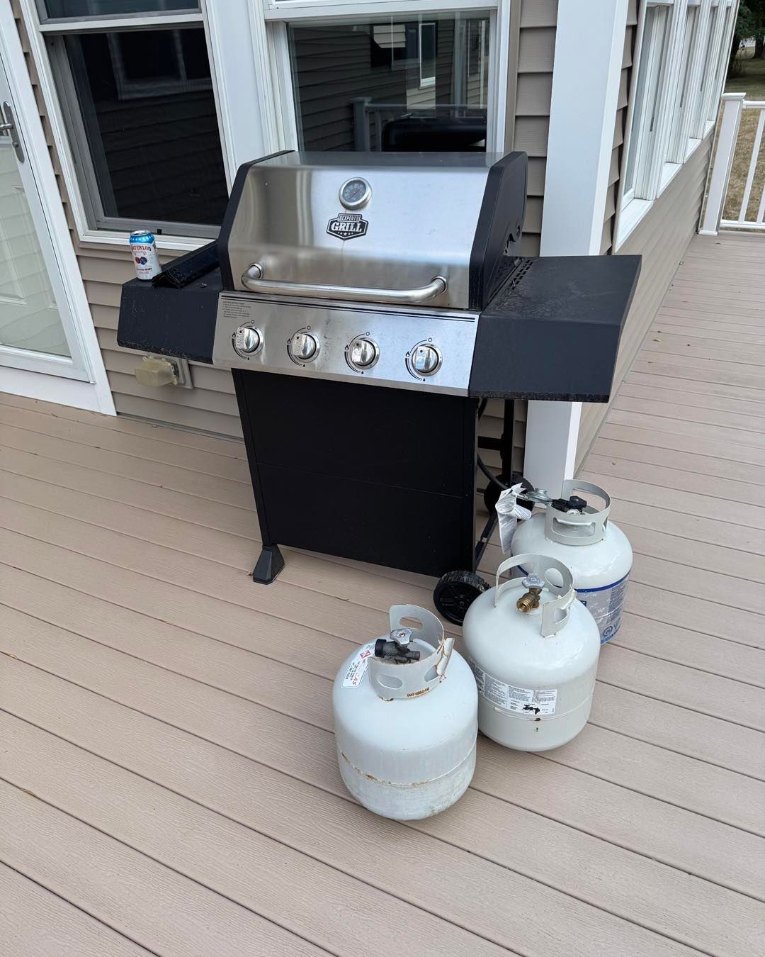 Gas grill on a deck with three propane tanks beside it.