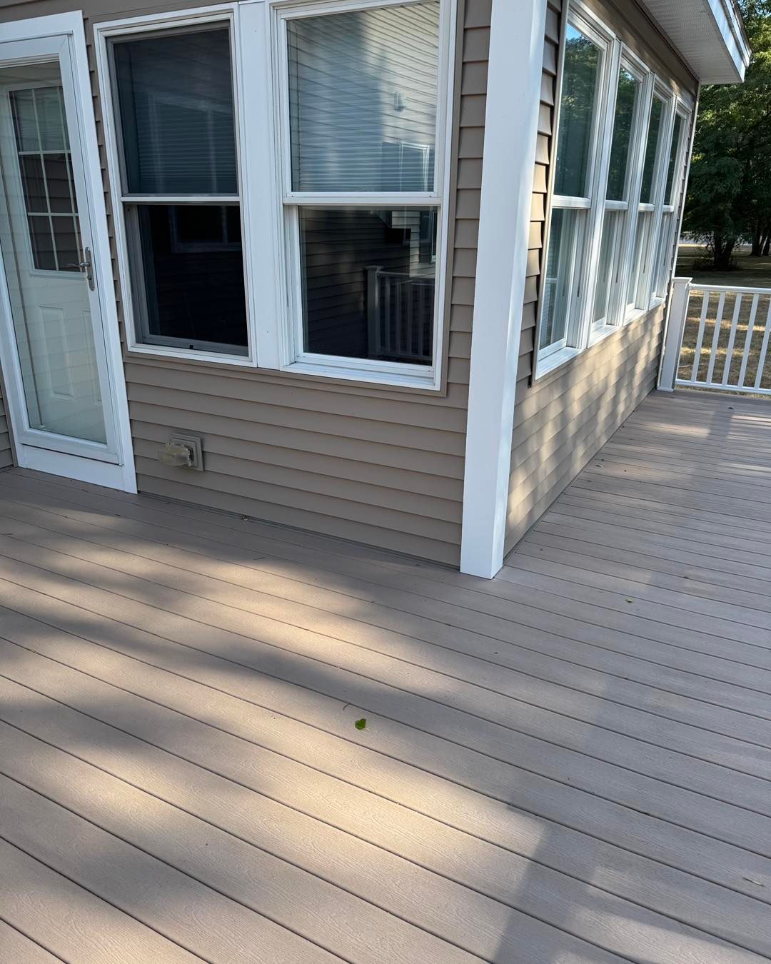 White house exterior with large windows and a beige wooden deck in sunlight
