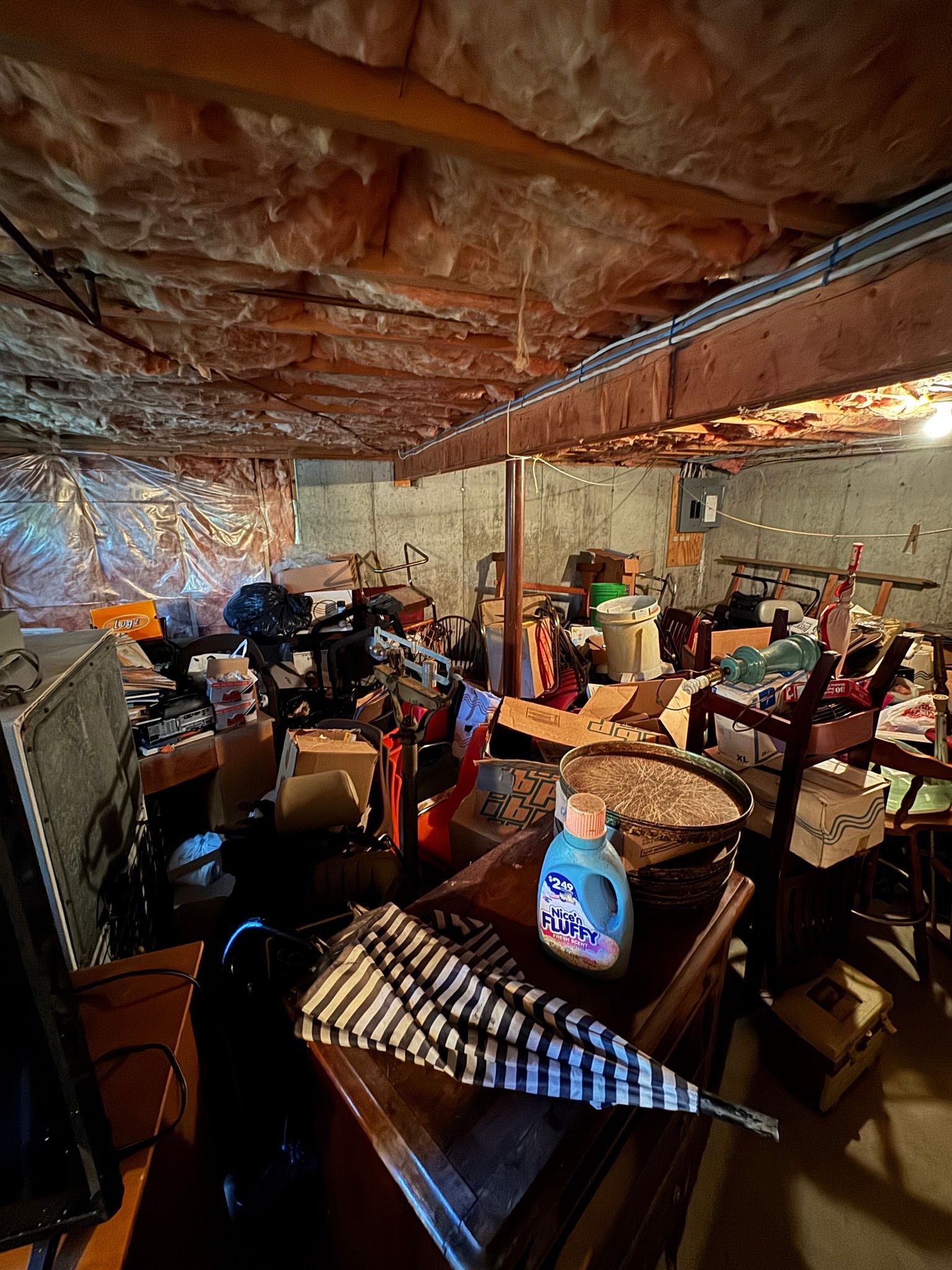 Cluttered basement storage room with shelves, boxes, tools, and a low brick ceiling under warm light