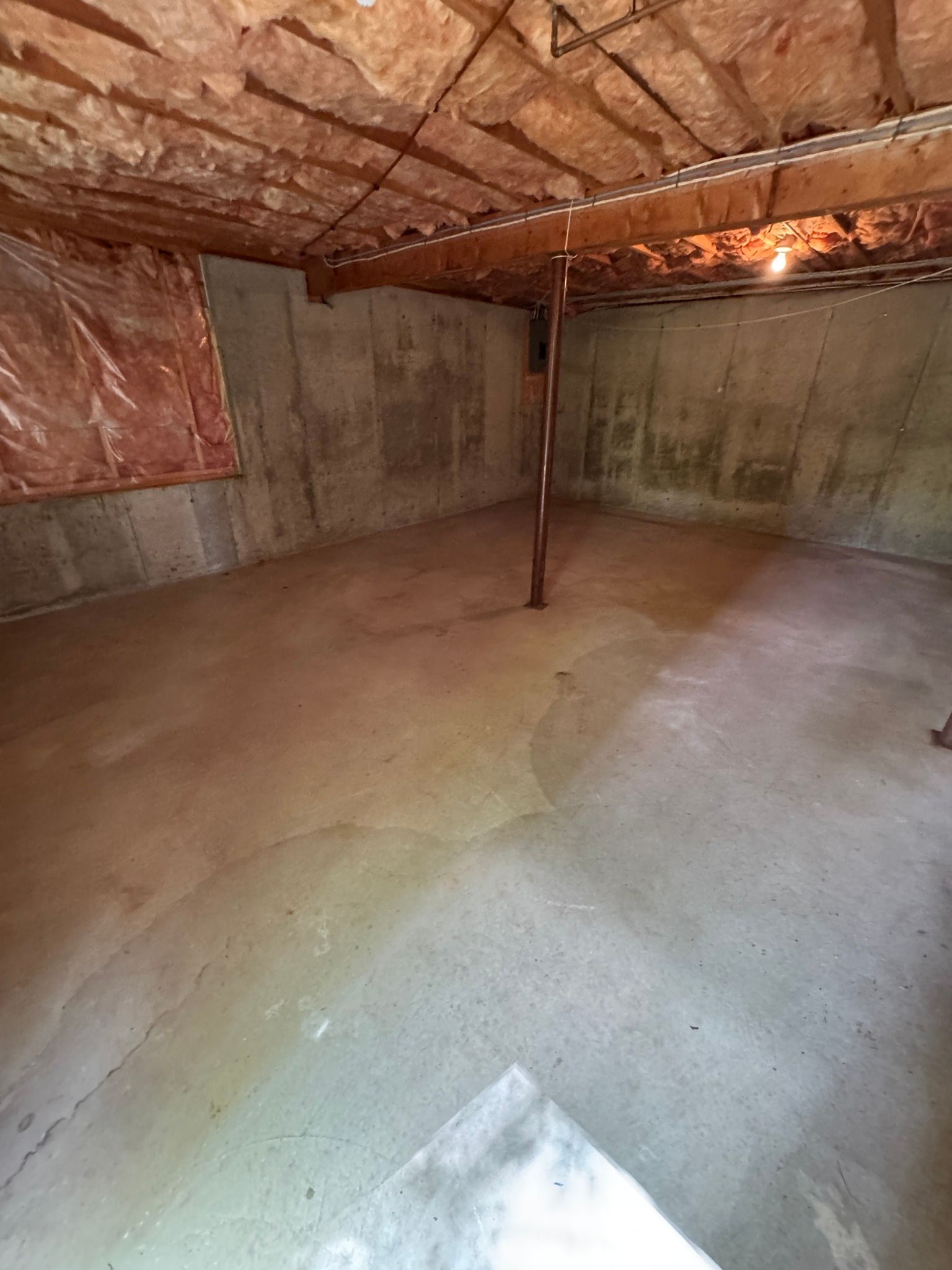 Empty unfinished basement with concrete floor, bare walls, exposed insulation, and a support post.