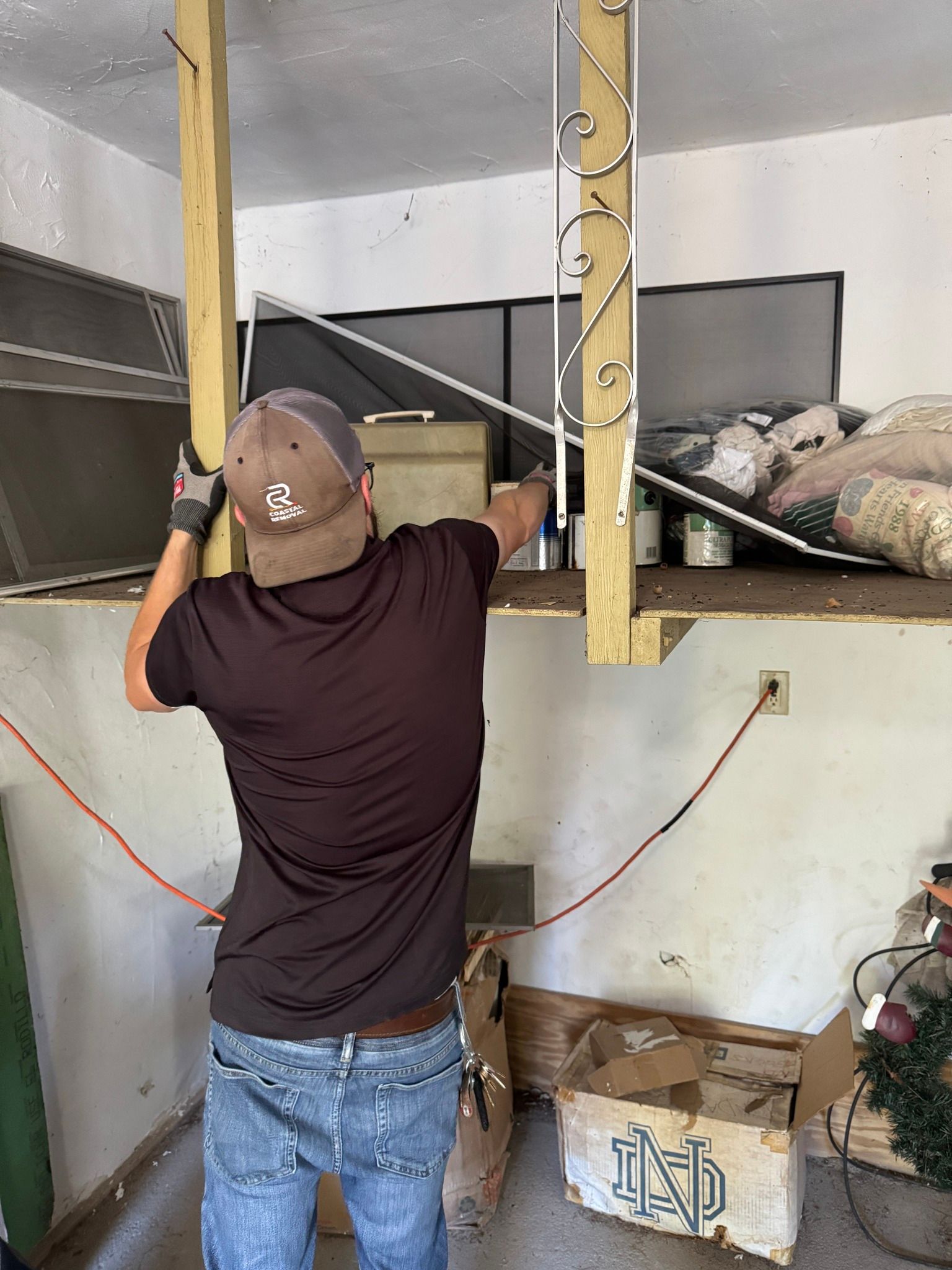 Person in a brown cap measuring a wall opening inside an unfinished room with exposed framing.