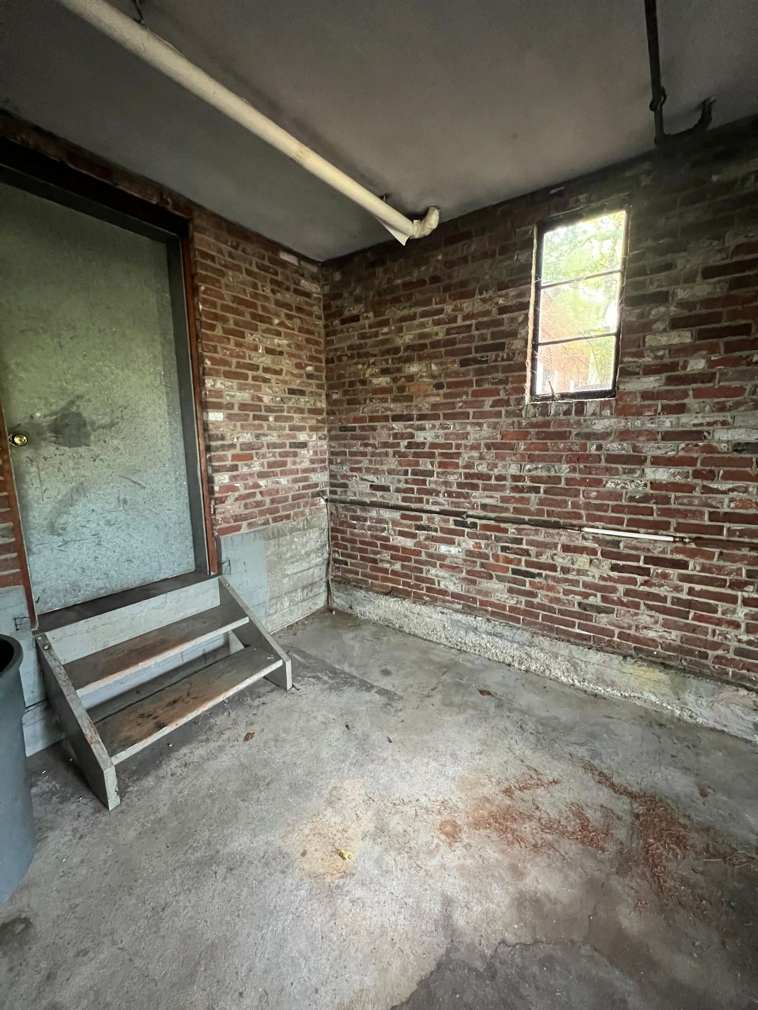 Empty brick garage with a frosted glass door, small window, and concrete floor.