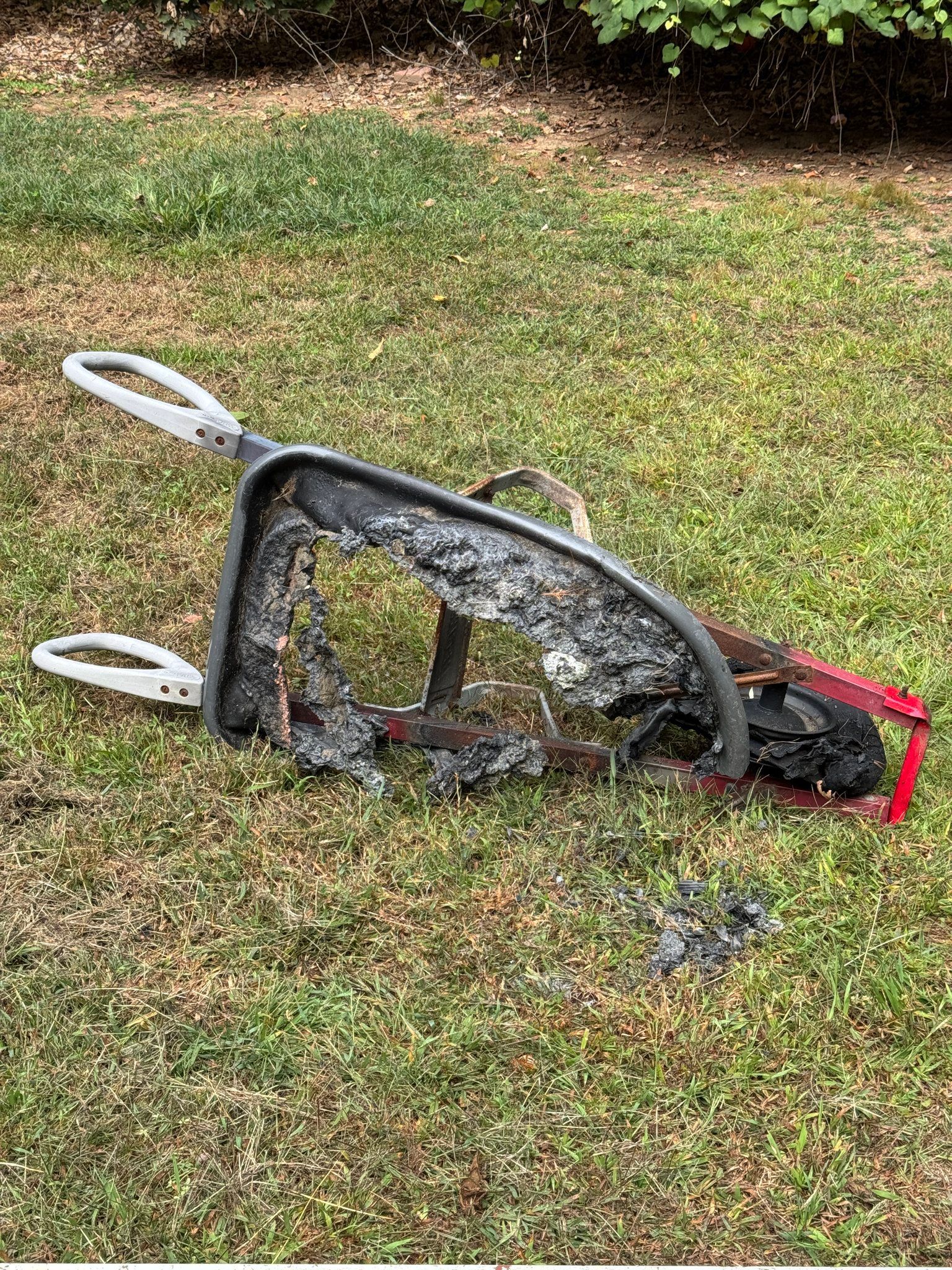 A tipped-over black and red folding cart lying on grass with two white wheels visible.
