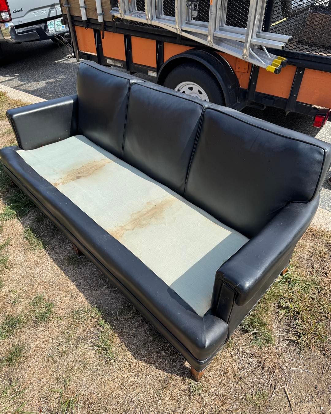Black vinyl couch with a light gray seat, sitting outdoors in a grassy lot.