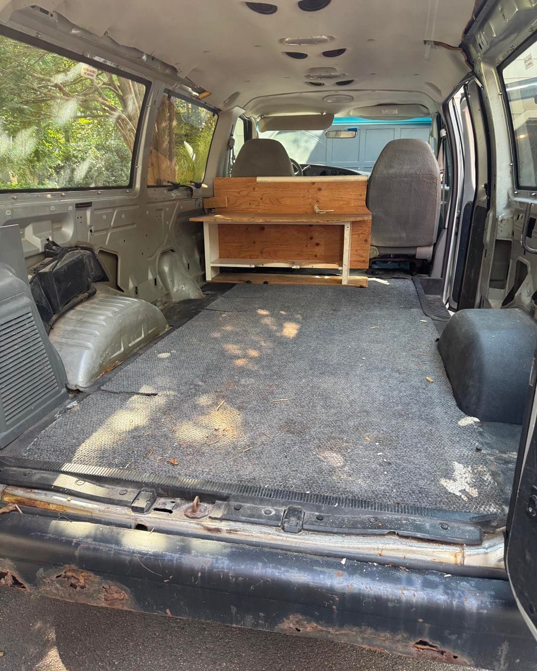 Interior of a stripped van with carpeted floor and wooden storage cabinet near the front seats
