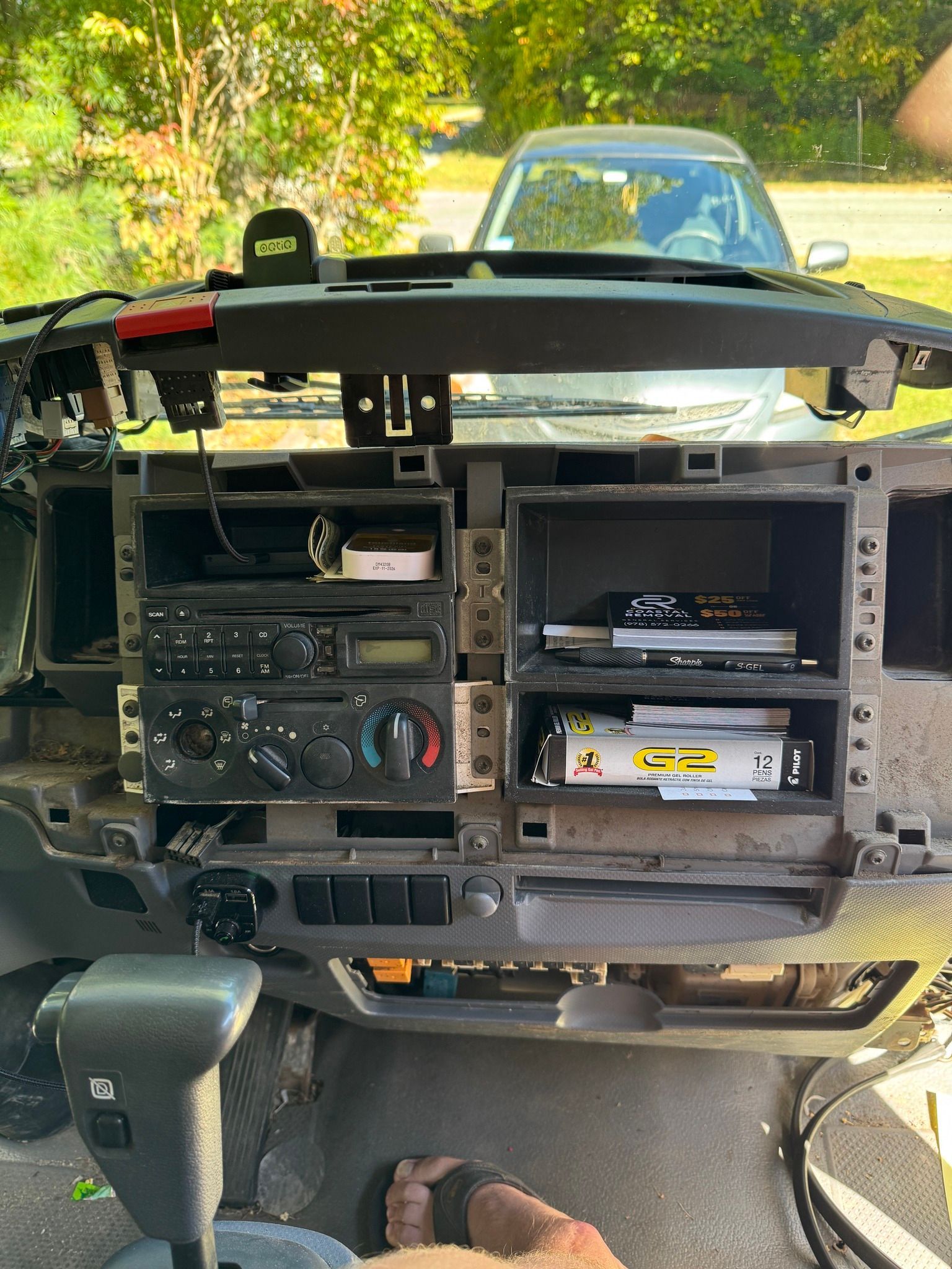 Car dashboard with center console removed, exposing radio and electronics; parked outdoors.