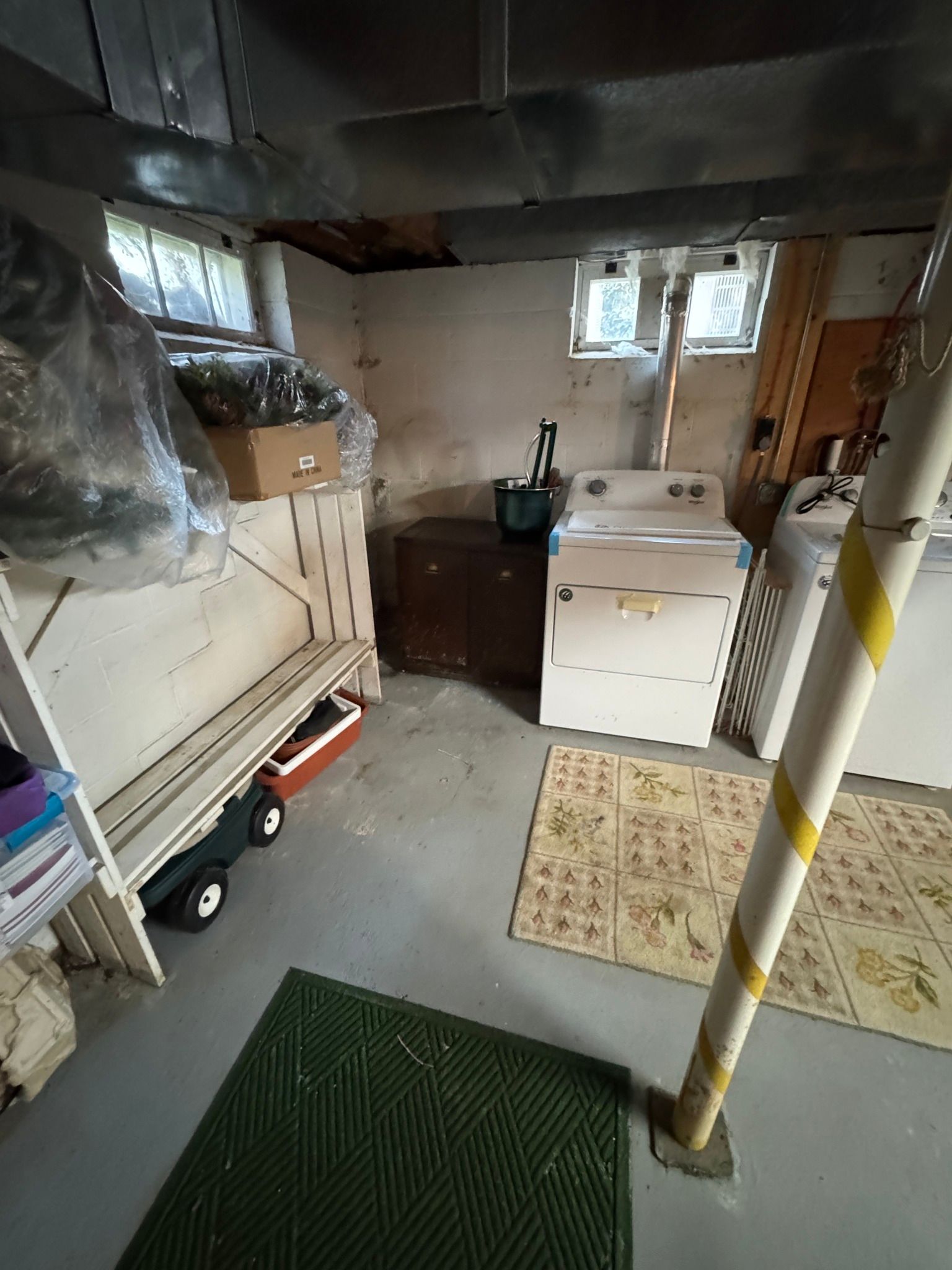 Basement utility room with washer, sink, dryer, storage, and a support pole on a carpeted floor