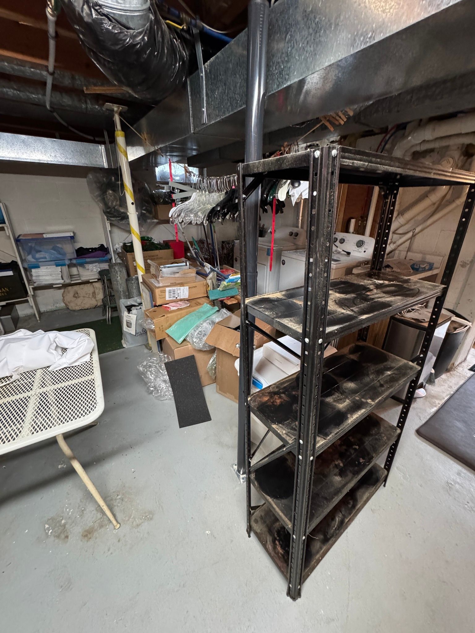 Cluttered basement storage area with metal shelves, cardboard boxes, and household items under exposed beams