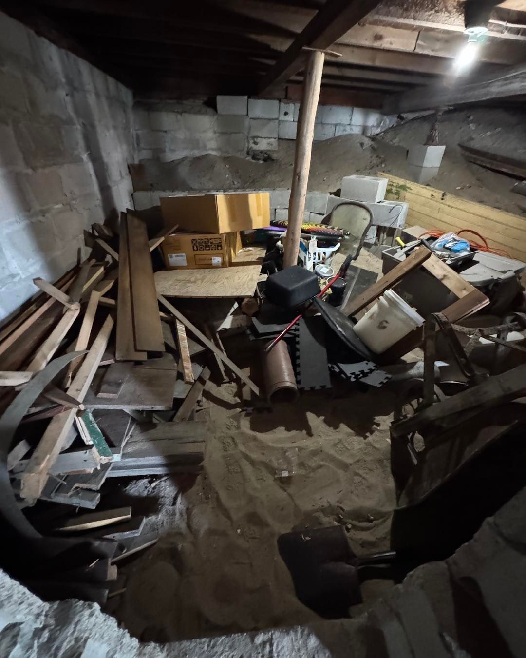 Cluttered basement with scattered wood, boxes, and debris around a central support post.