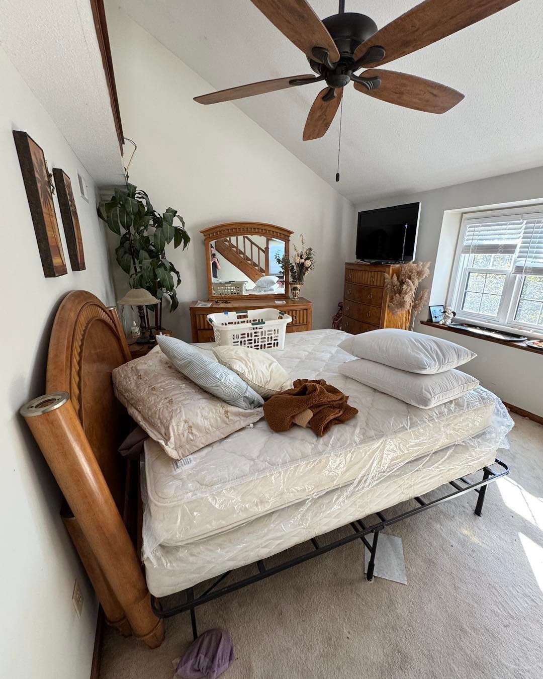 Bright bedroom with wooden bed, dresser, ceiling fan, TV, and window by a fireplace.