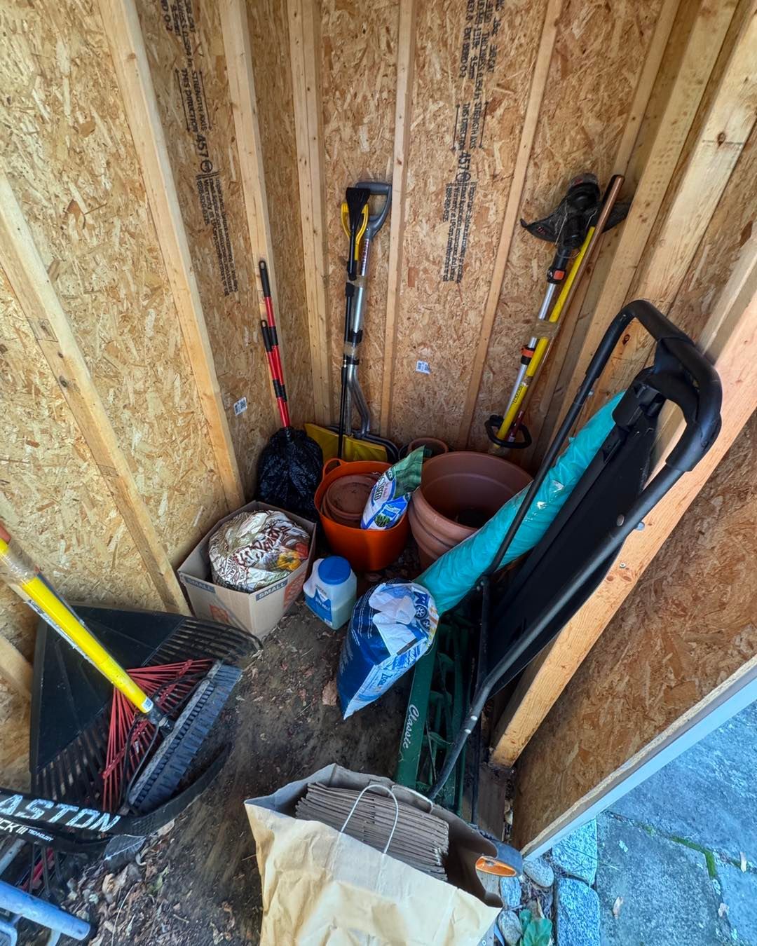 Tools and yard supplies stored in a small unfinished shed with wood walls and a blue door frame