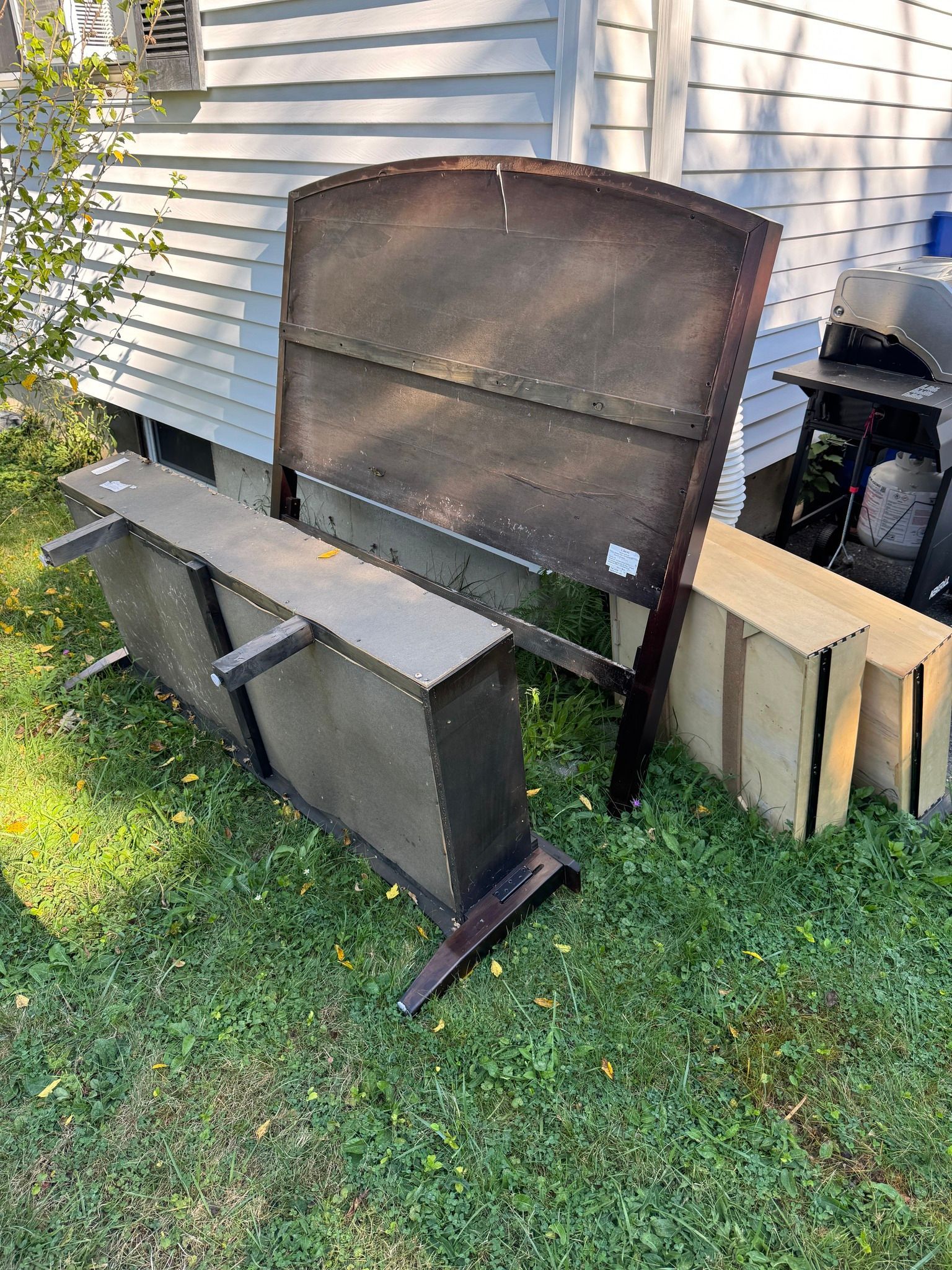 Rustic metal outdoor bench and upright panel on grass beside a house wall.