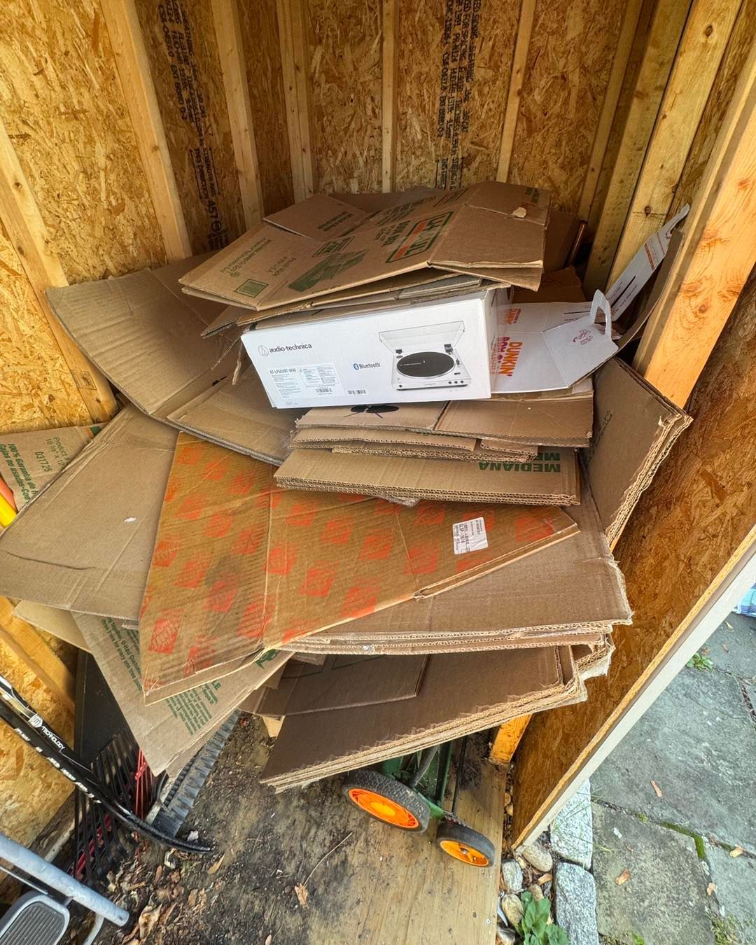 Stack of flattened cardboard boxes inside a wooden bin, with a white product box on top.