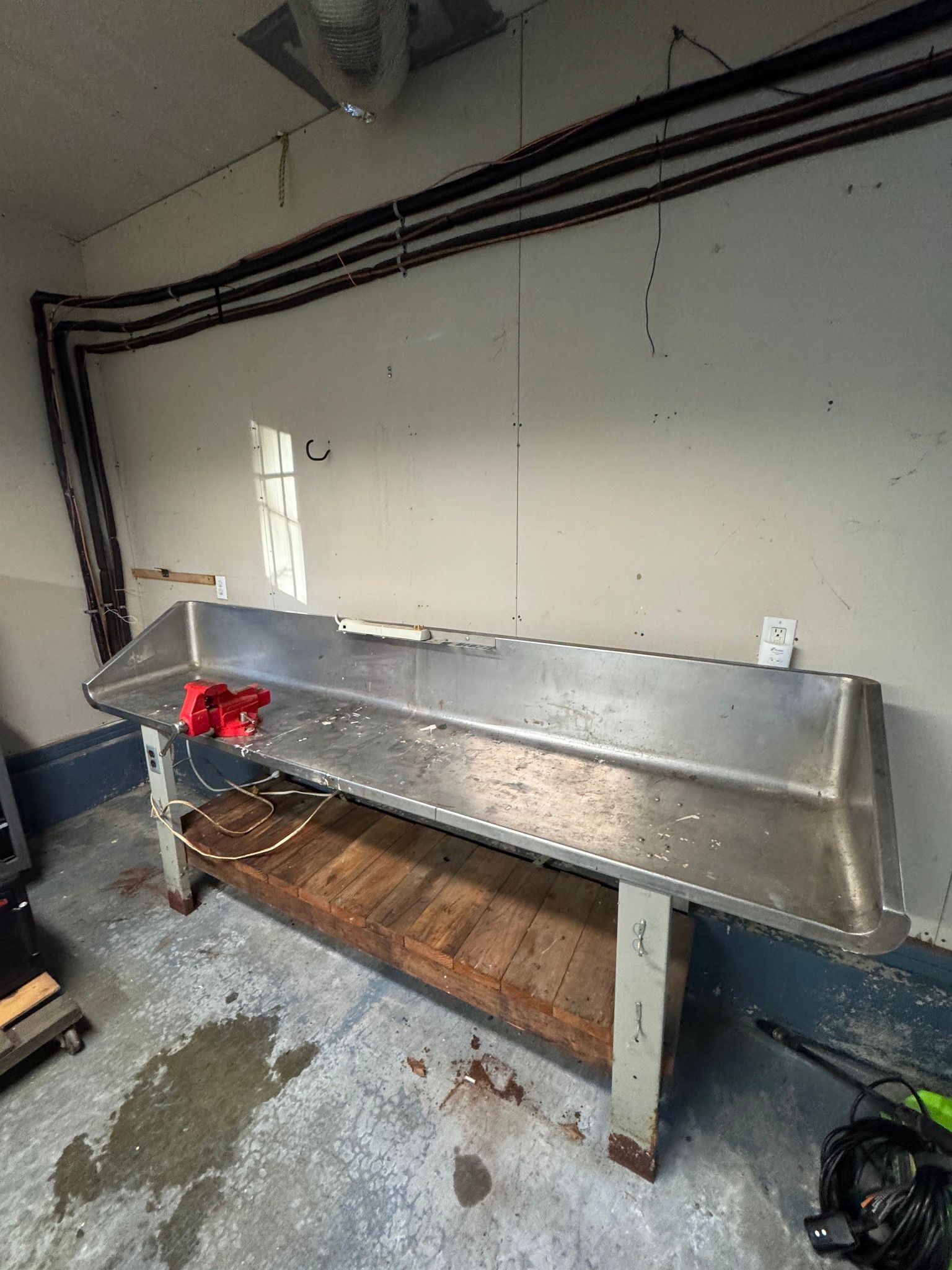 Long metal workbench in a garage with red clamps and pipes along the wall