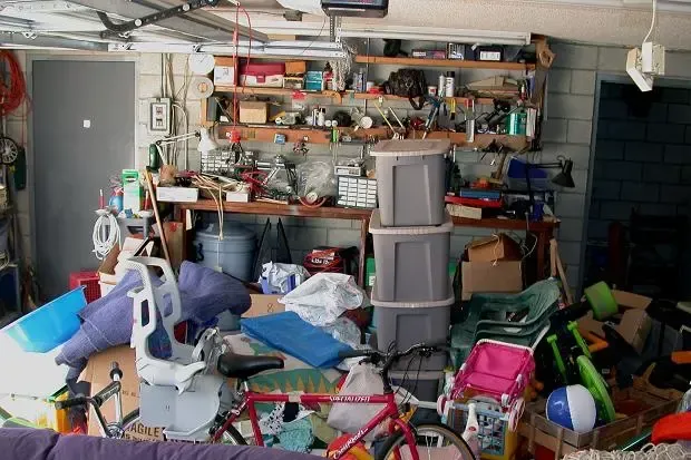 Cluttered garage packed with tools, bins, boxes, and assorted household items stacked on shelves and floor