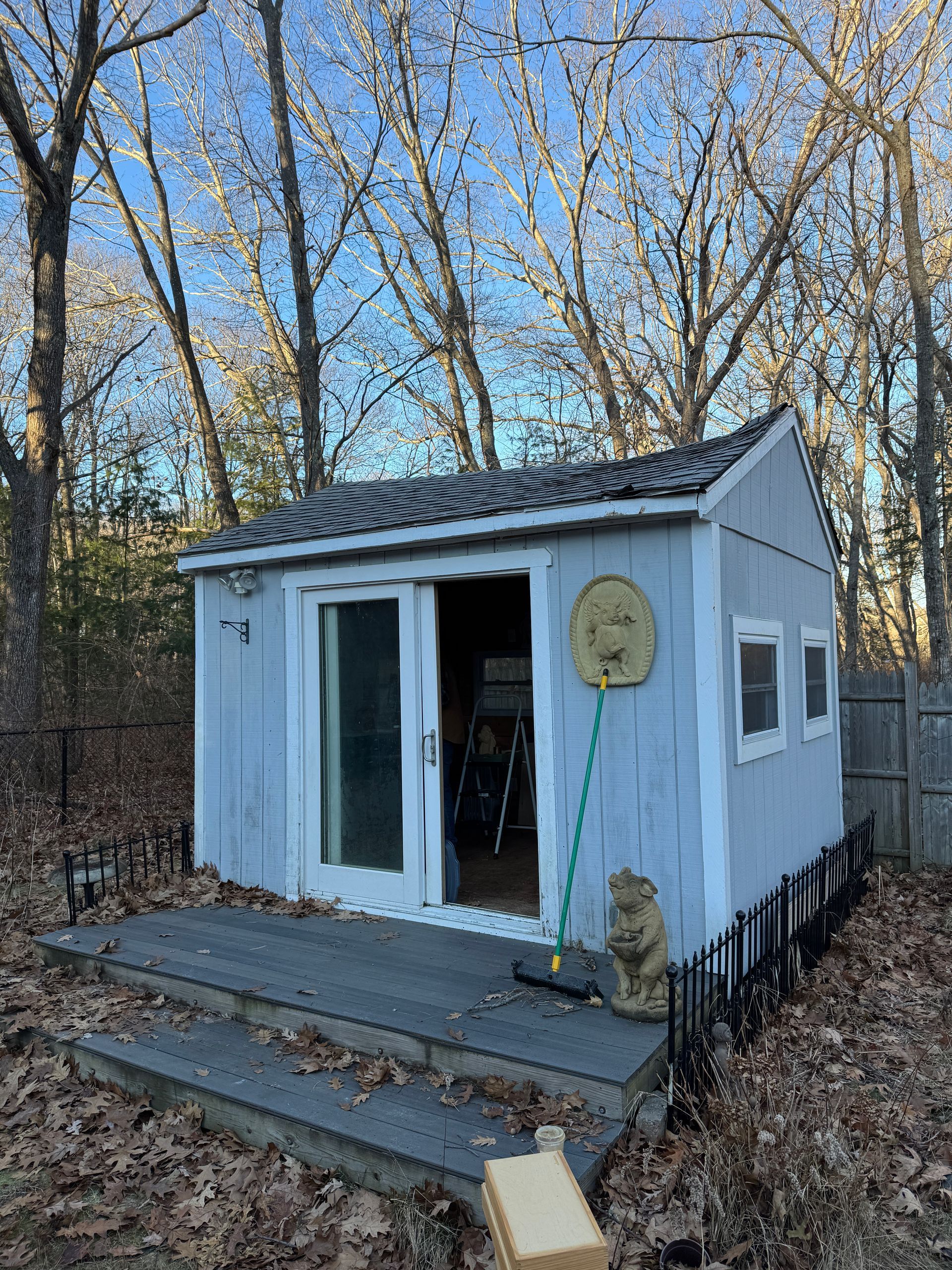 Small white backyard shed with open sliding doors, steps, and a leafless wooded backdrop.