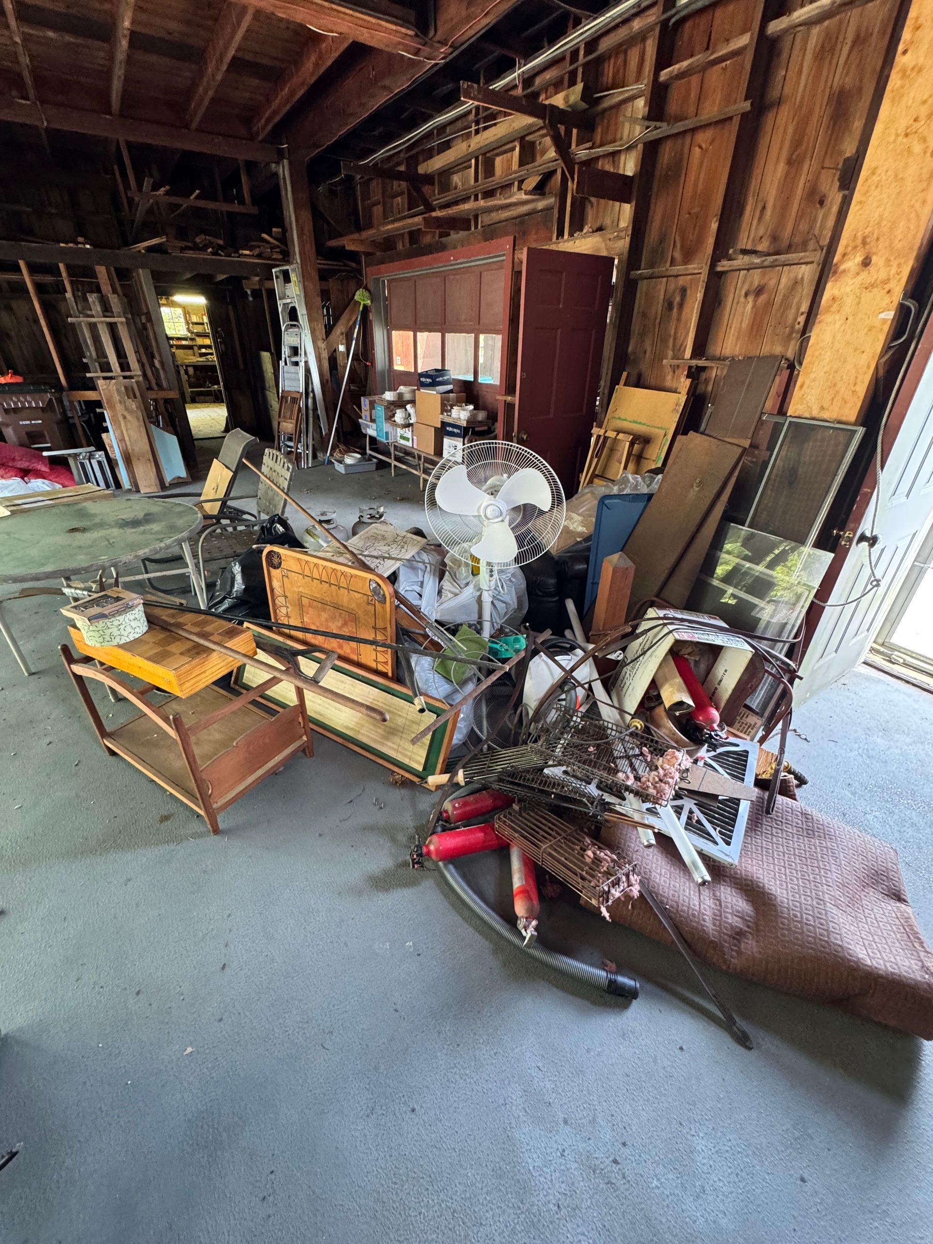 Cluttered, damaged room with debris, furniture, and exposed wooden walls after heavy fire or flooding
