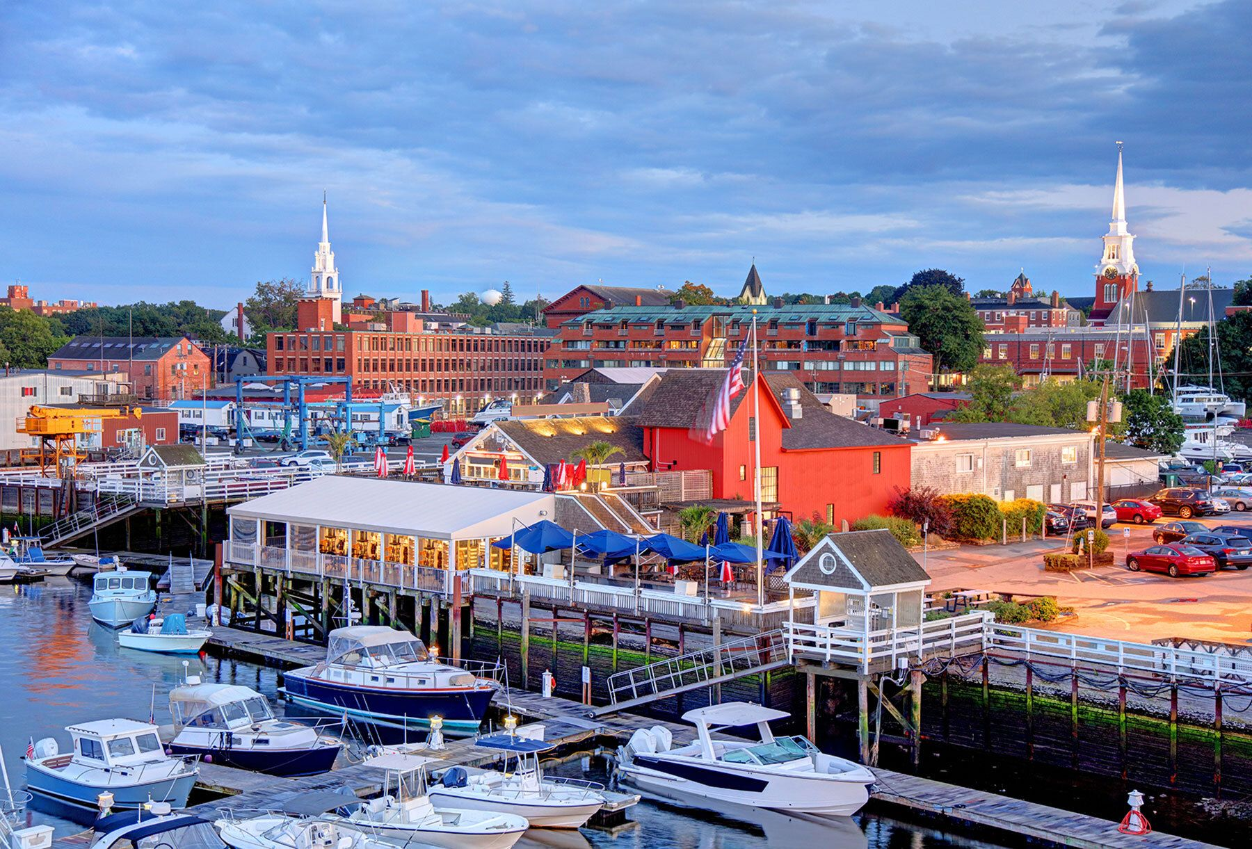 Harbor town with boats, waterfront buildings, and church spires under a blue sky