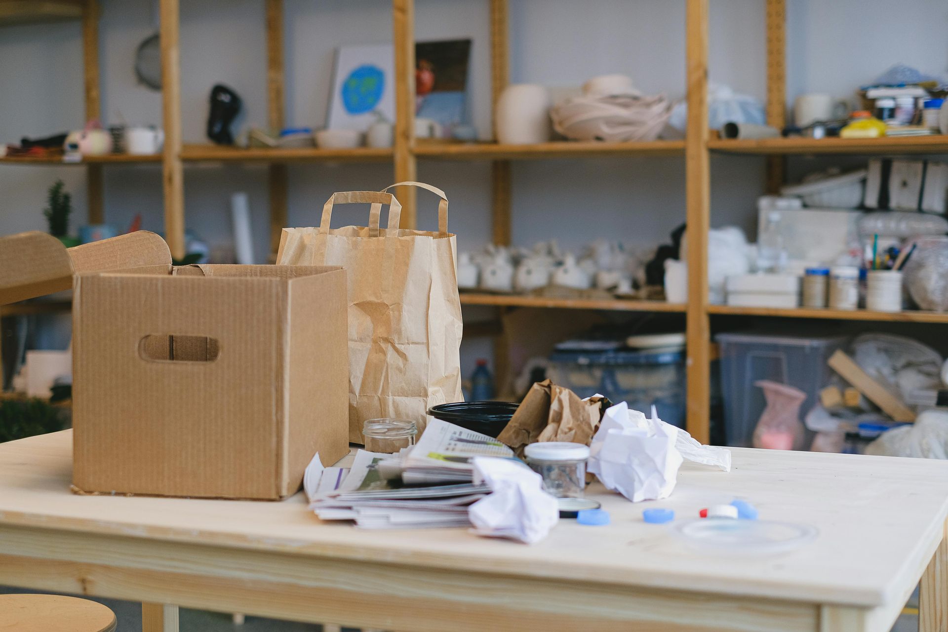 Paper bags and boxes on a table in a craft studio with shelves of supplies in the background