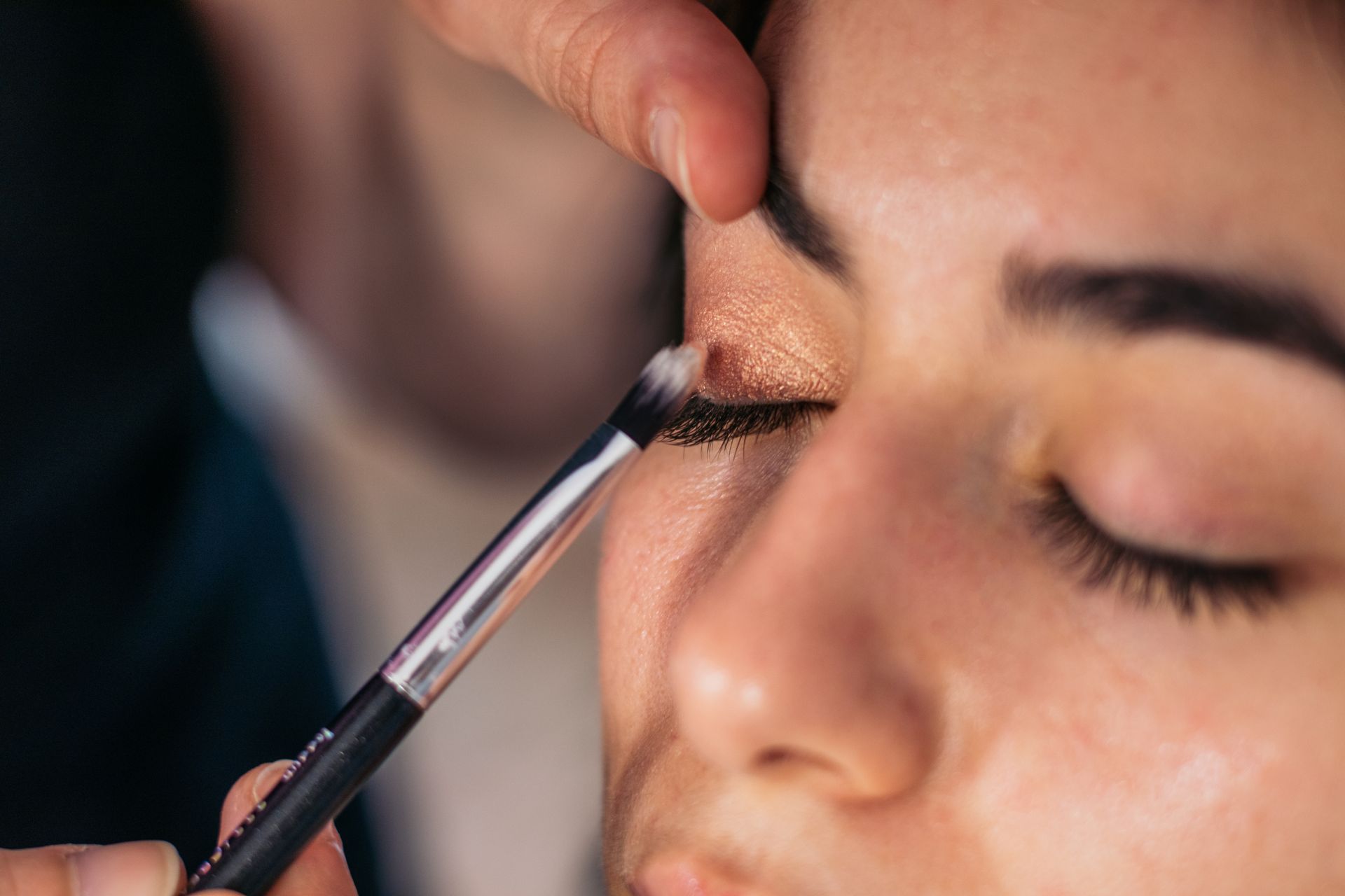 Makeup artist applying eyeshadow to a closed eyelid with a brush