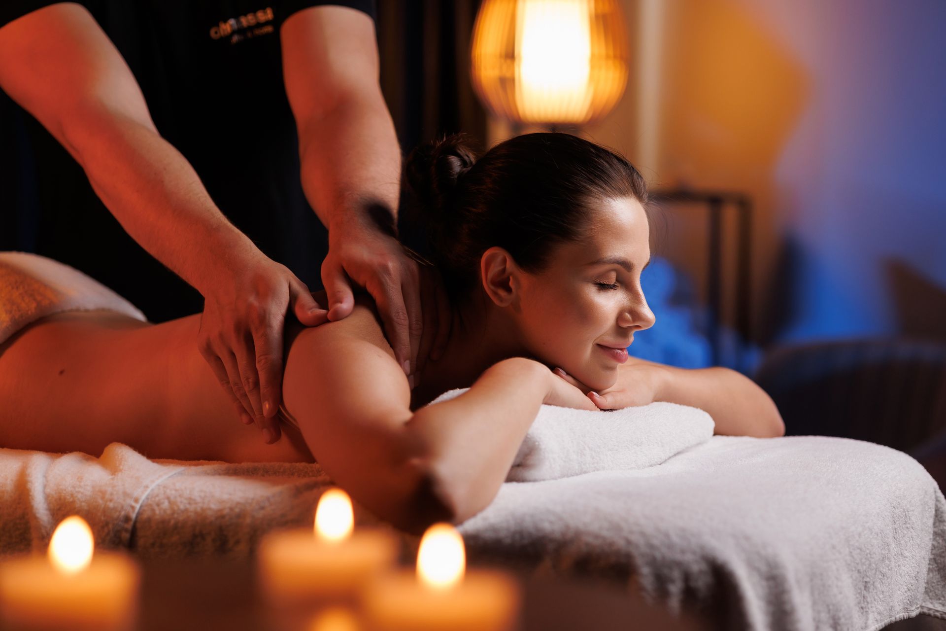 Client receiving a back massage in a dimly lit spa with candles and warm orange lighting
