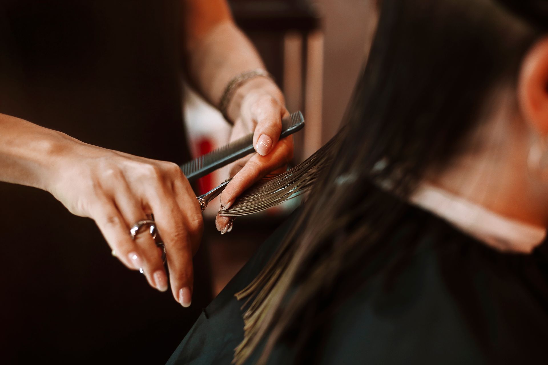 Stylist trimming dark hair with scissors and comb in a salon setting