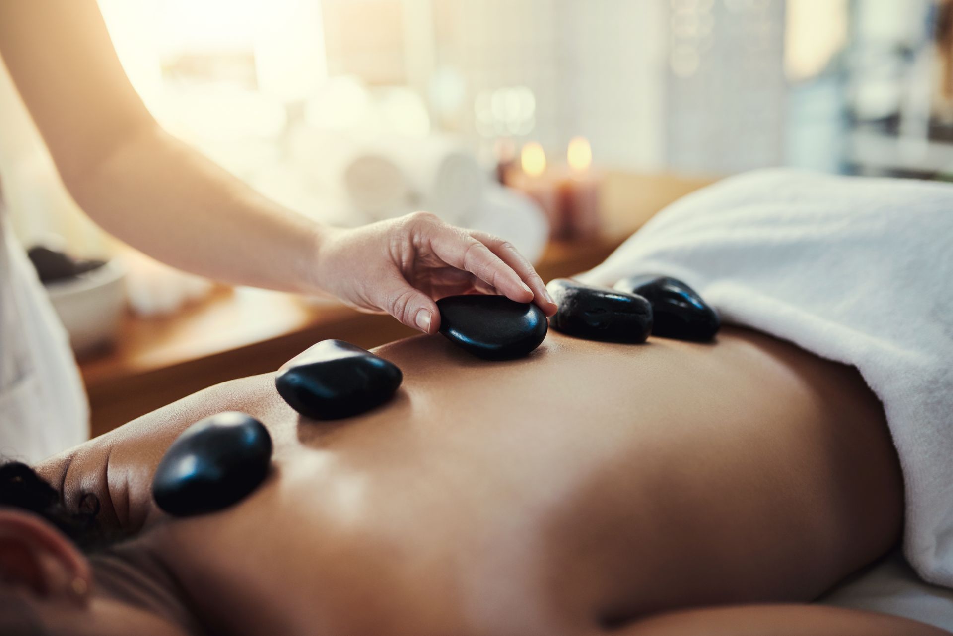 Hot stone massage with stones placed on a person’s back while a therapist presses one stone