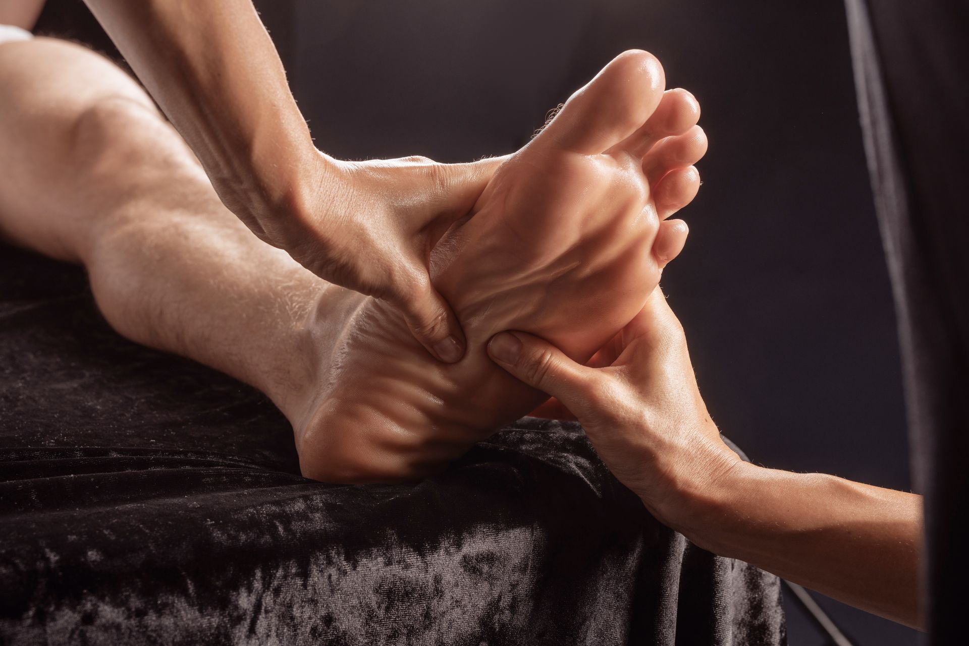 Close-up of hands holding and massaging a bare foot on a dark towel
