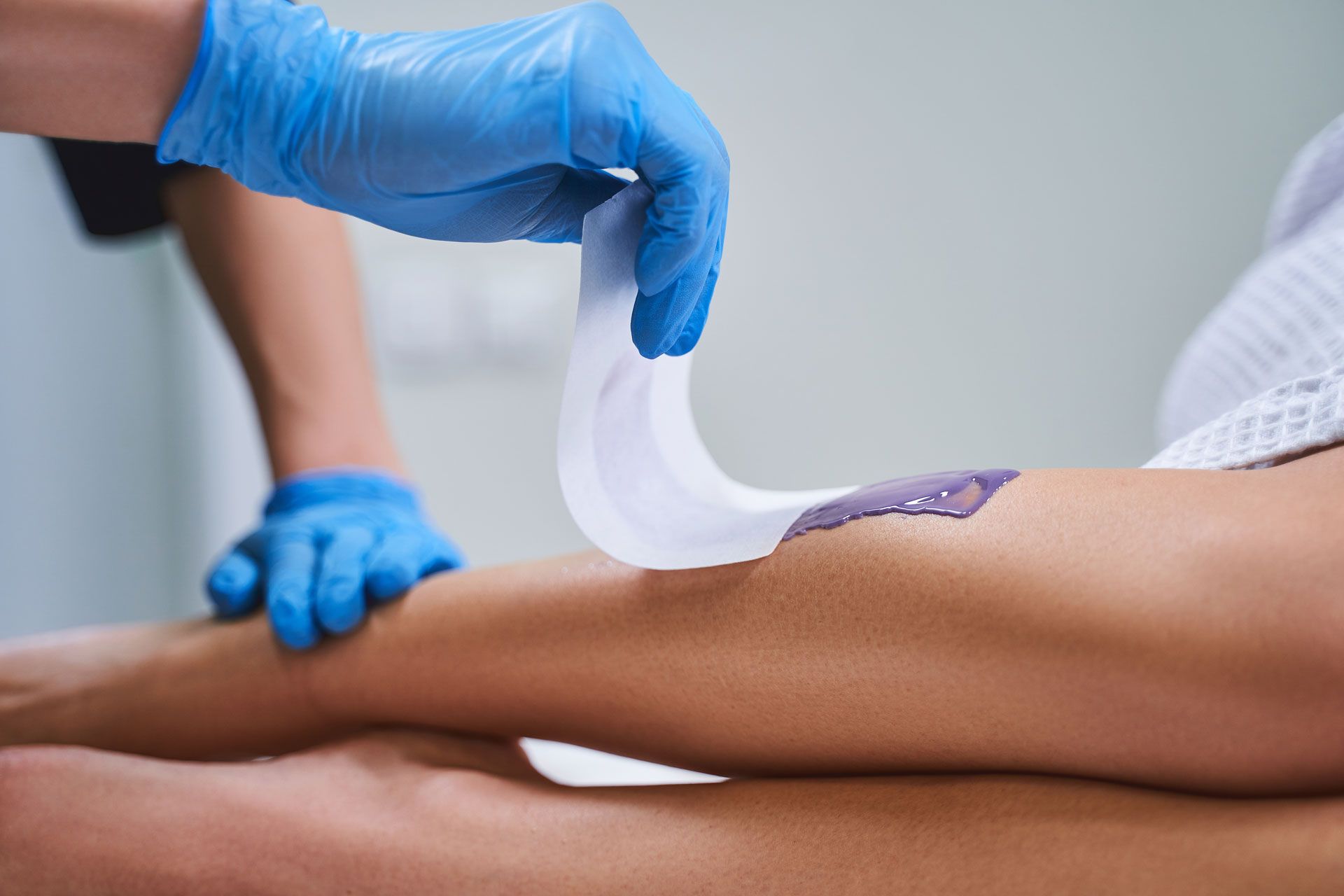 Gloved hands applying wax strip to a client’s leg during hair removal treatment