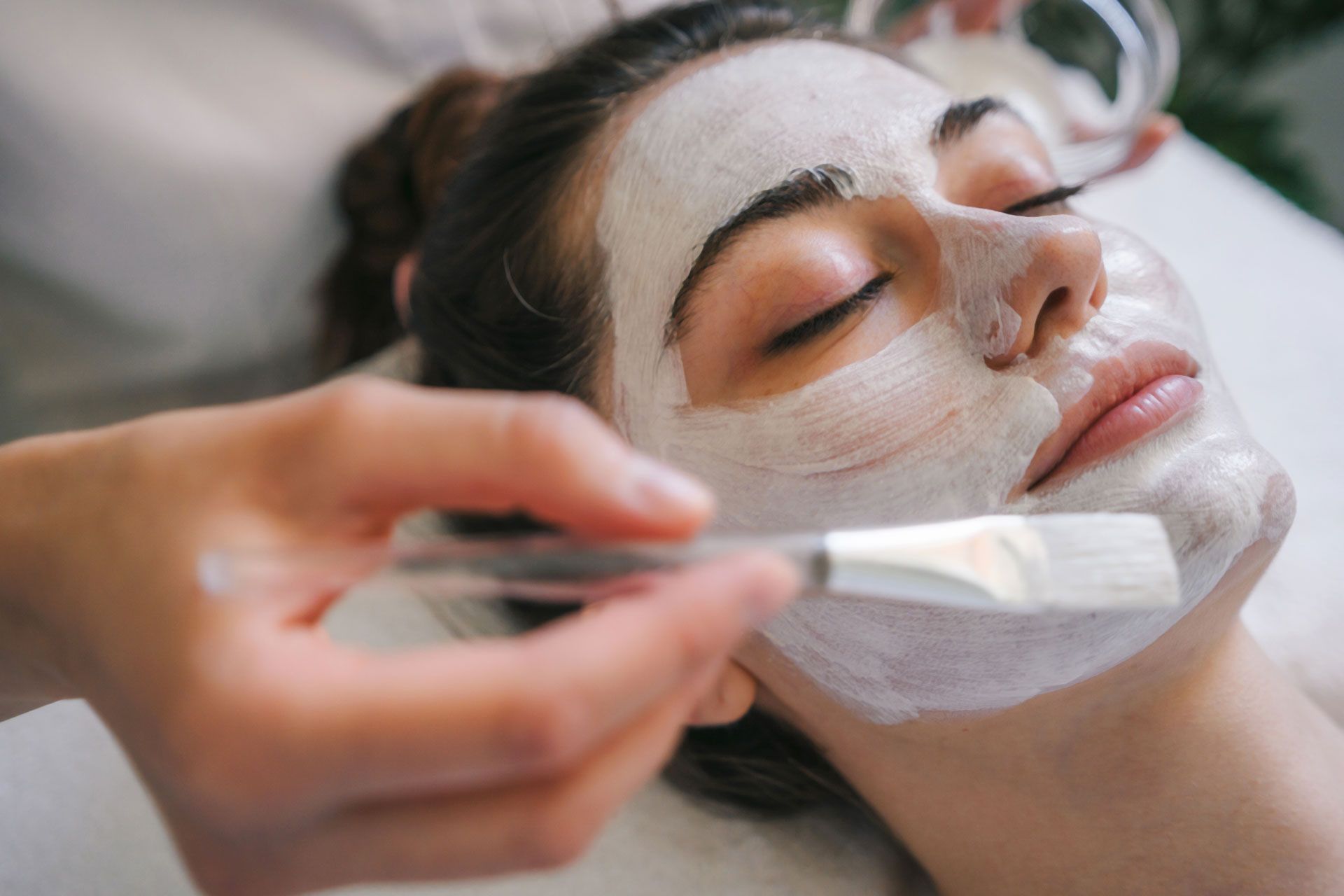 Spa facial treatment with a brush applying white cream to a woman’s face