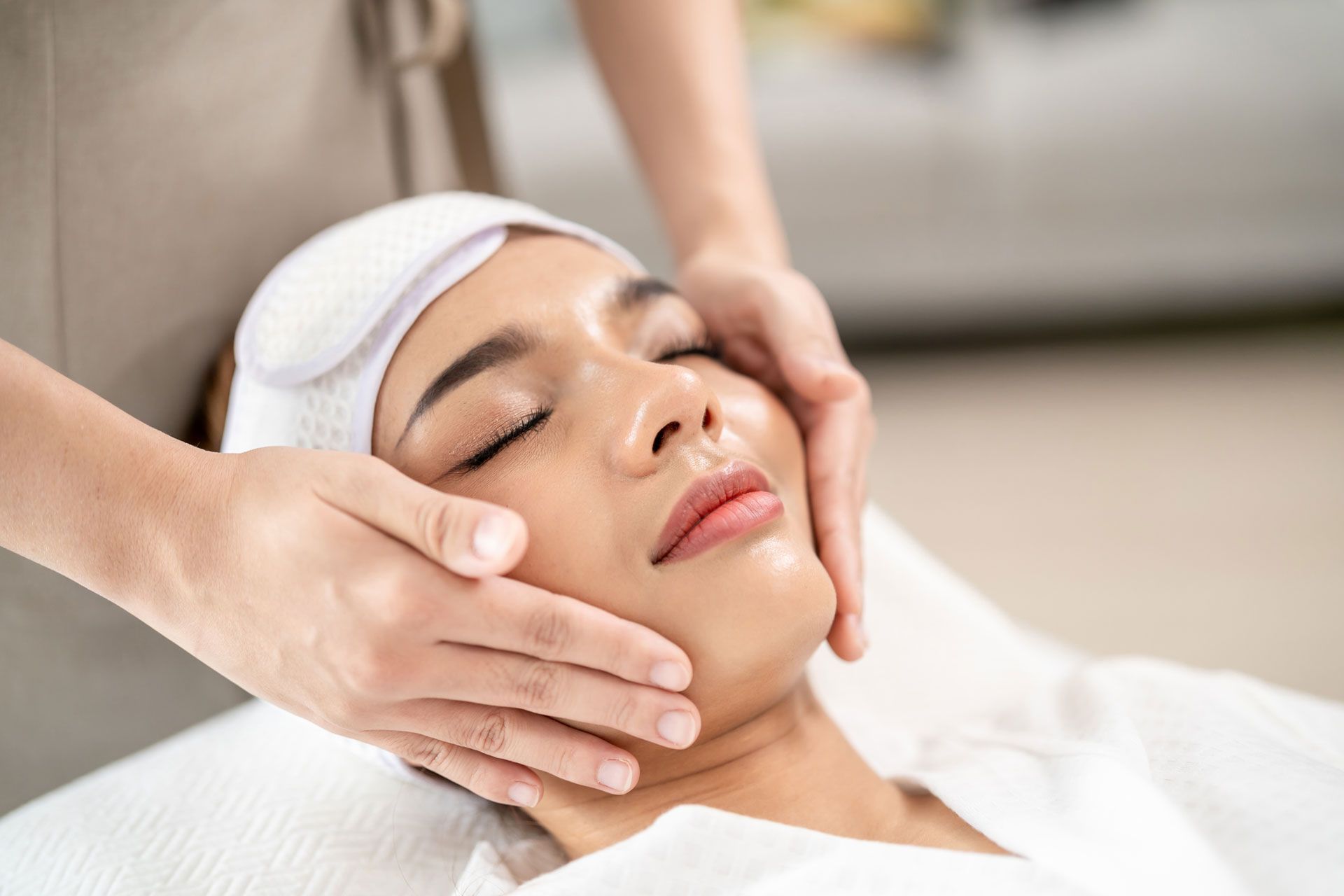 Spa therapist giving a facial massage to a relaxed client with a white headband