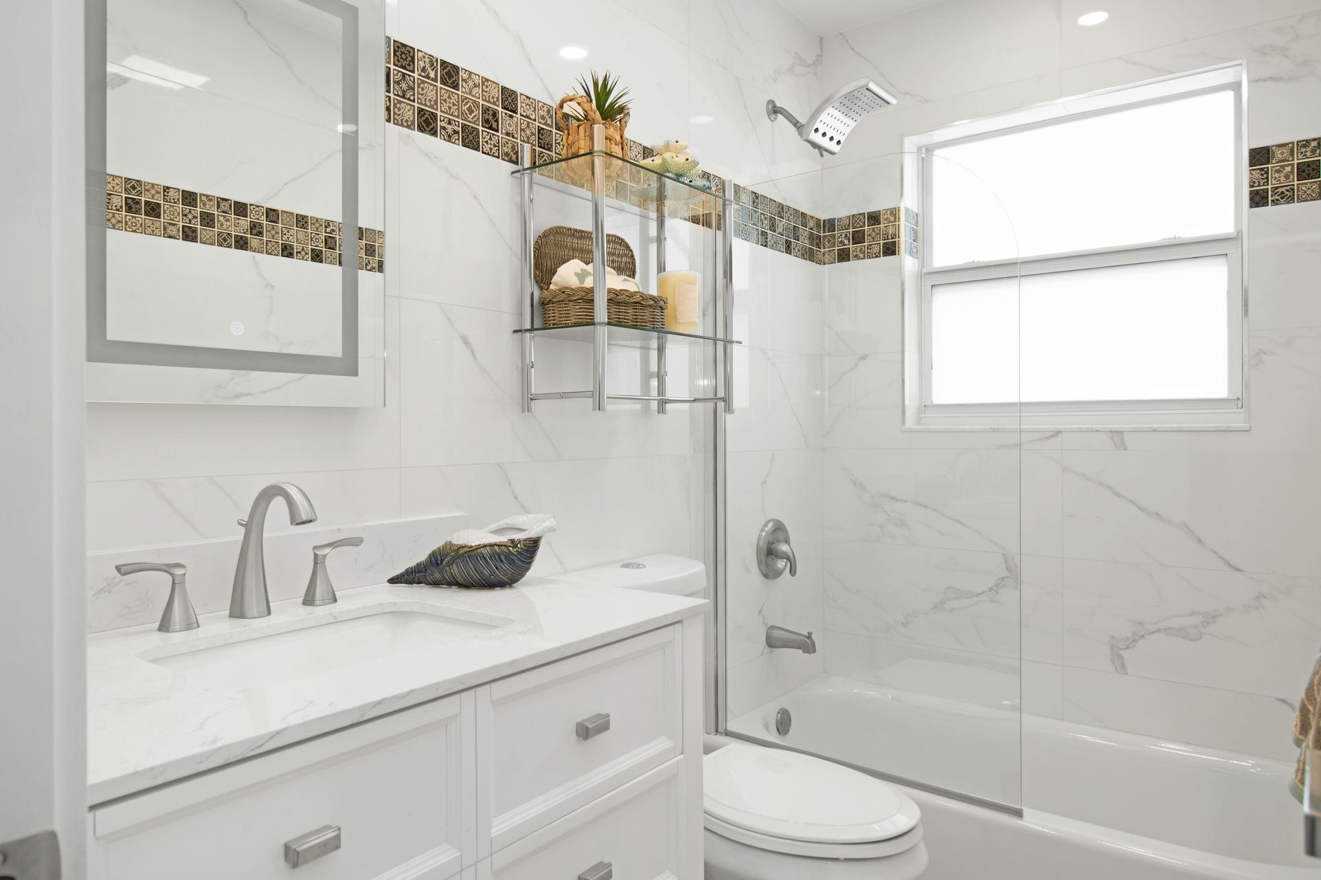 A bright bathroom with white marble-style walls, a white vanity, a mirror, a glass-enclosed shower, and a toilet.