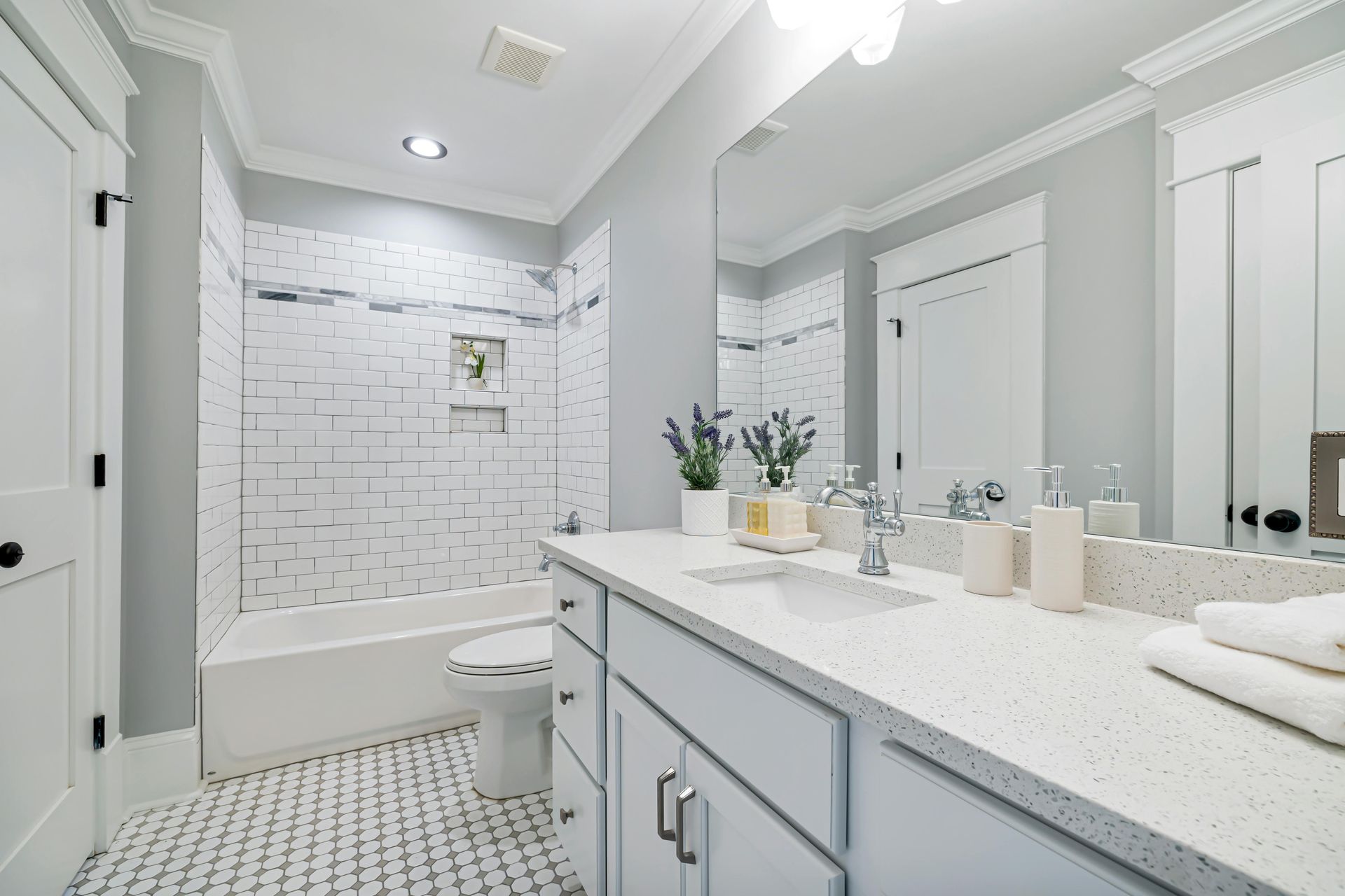 A bright bathroom featuring a white subway tile shower, a patterned tile floor, and a vanity with a light gray cabinet.