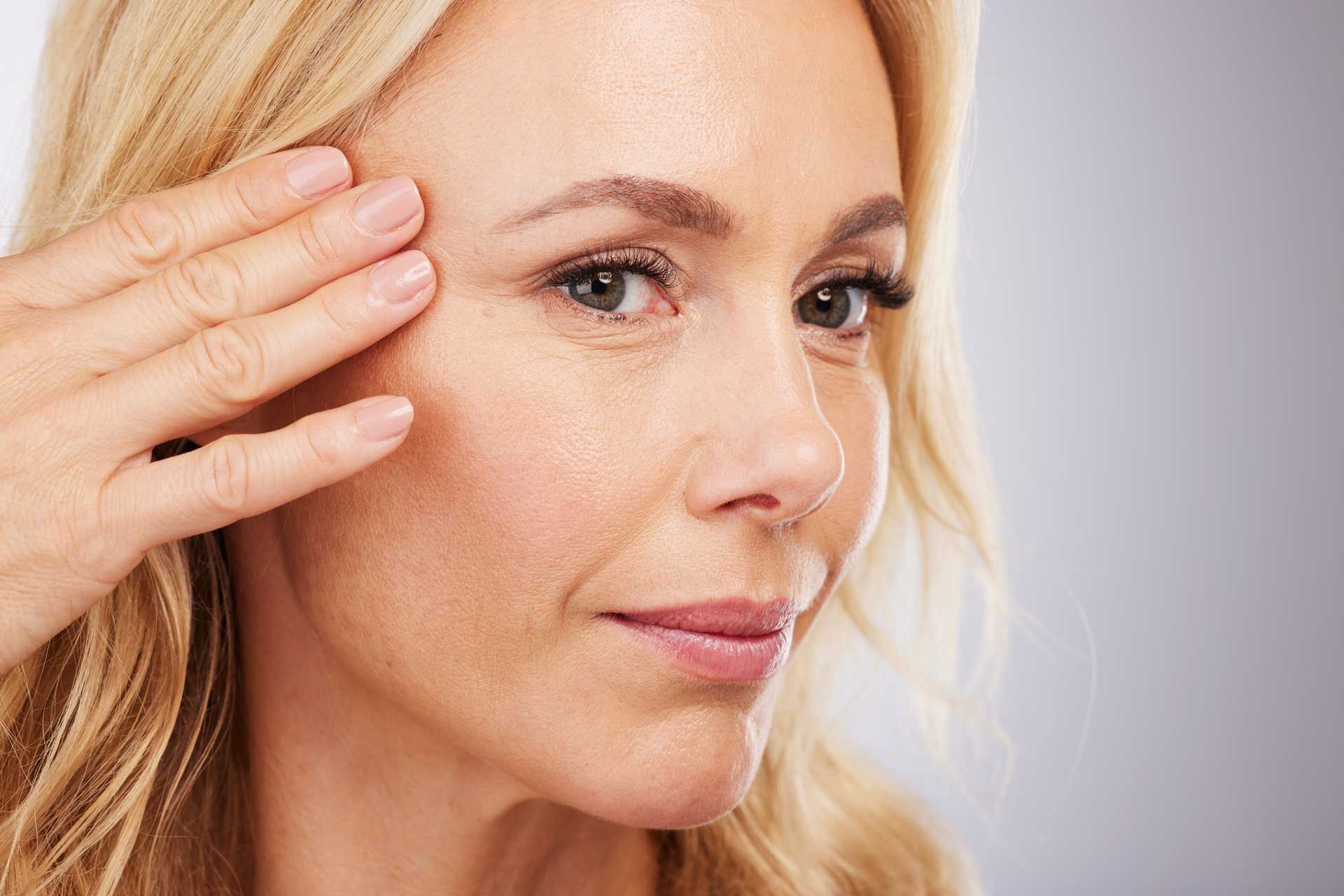 A woman is touching her face with her hand and looking at the camera.