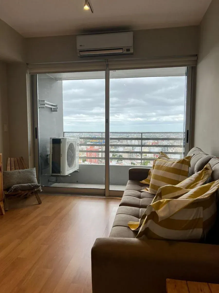 Sala de estar con sofá marrón, almohadas amarillas, puerta corrediza de vidrio, vista del paisaje urbano