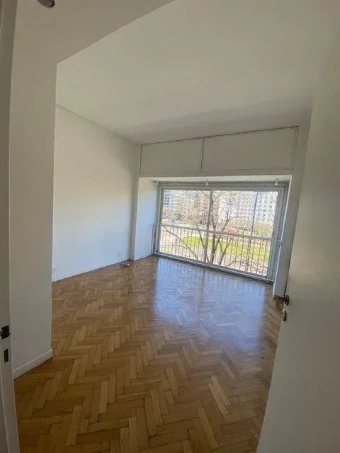 Habitación vacía con suelo de madera en espiga, ventana grande y paredes blancas.