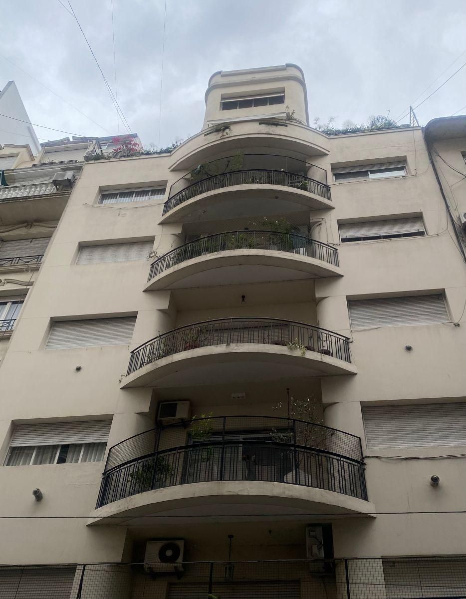 Edificio beige de varios pisos con balcones curvos y parte superior redondeada, bajo un cielo nublado.